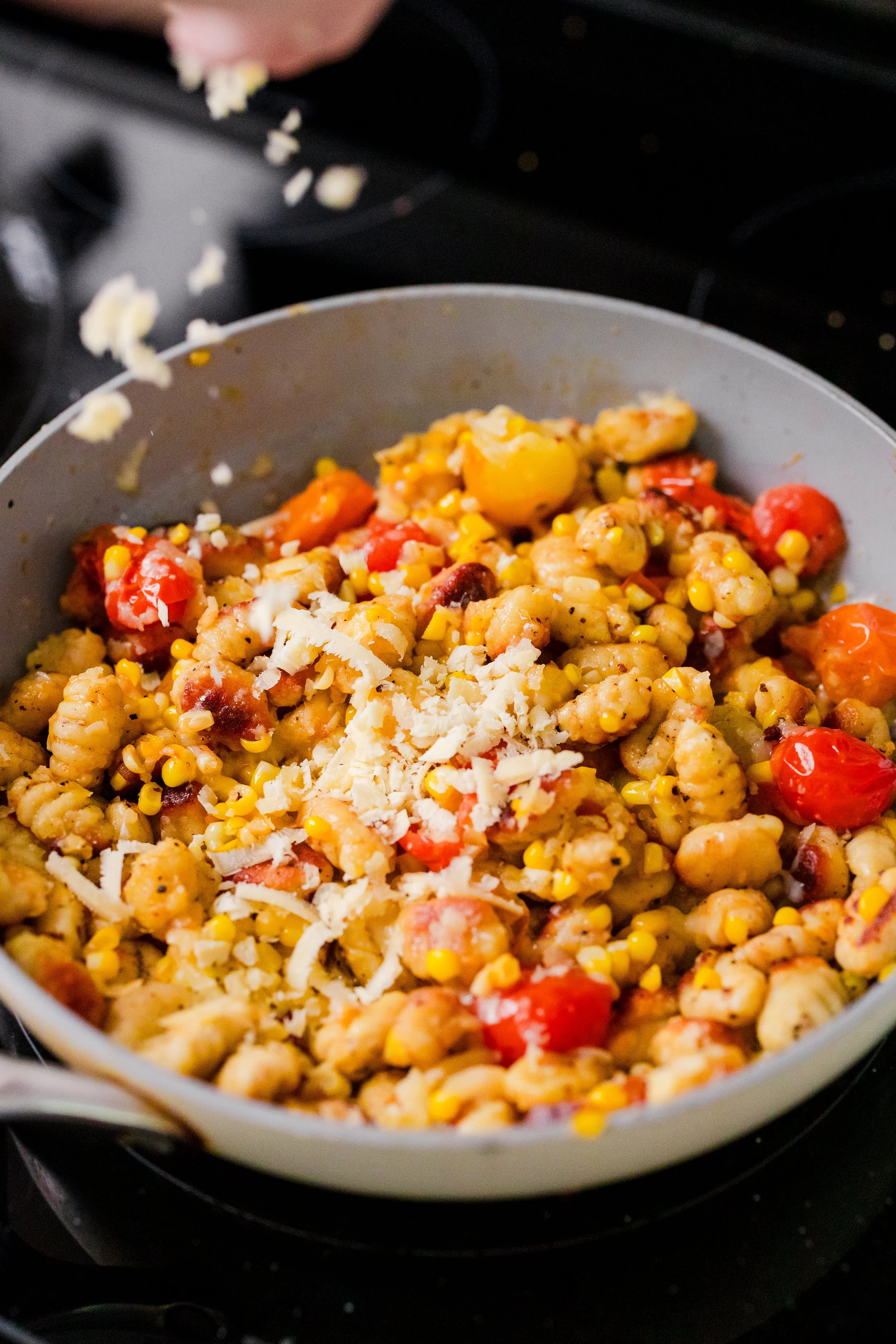 A skillet of cooked pasta mixed with cherry tomatoes, corn, and shredded cheese.