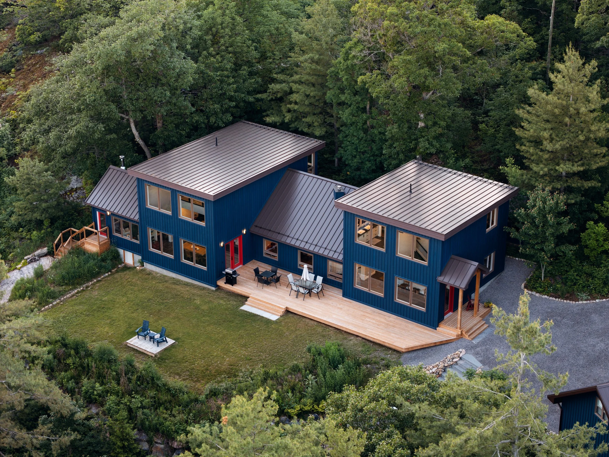Aerial view of a custom modern cottage built by Bredin Brothers, featuring blue vertical siding, standing seam metal roofing, expansive wood decking and contemporary architecture.