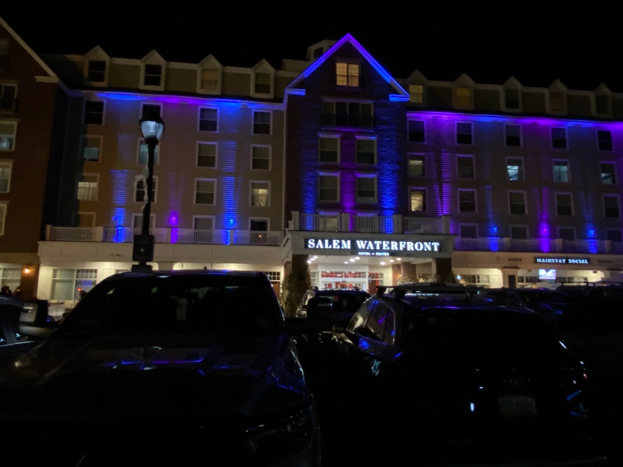 Nighttime view of a multi-story hotel named Salem Waterfront, illuminated with purple and blue lights, with cars parked in the foreground.