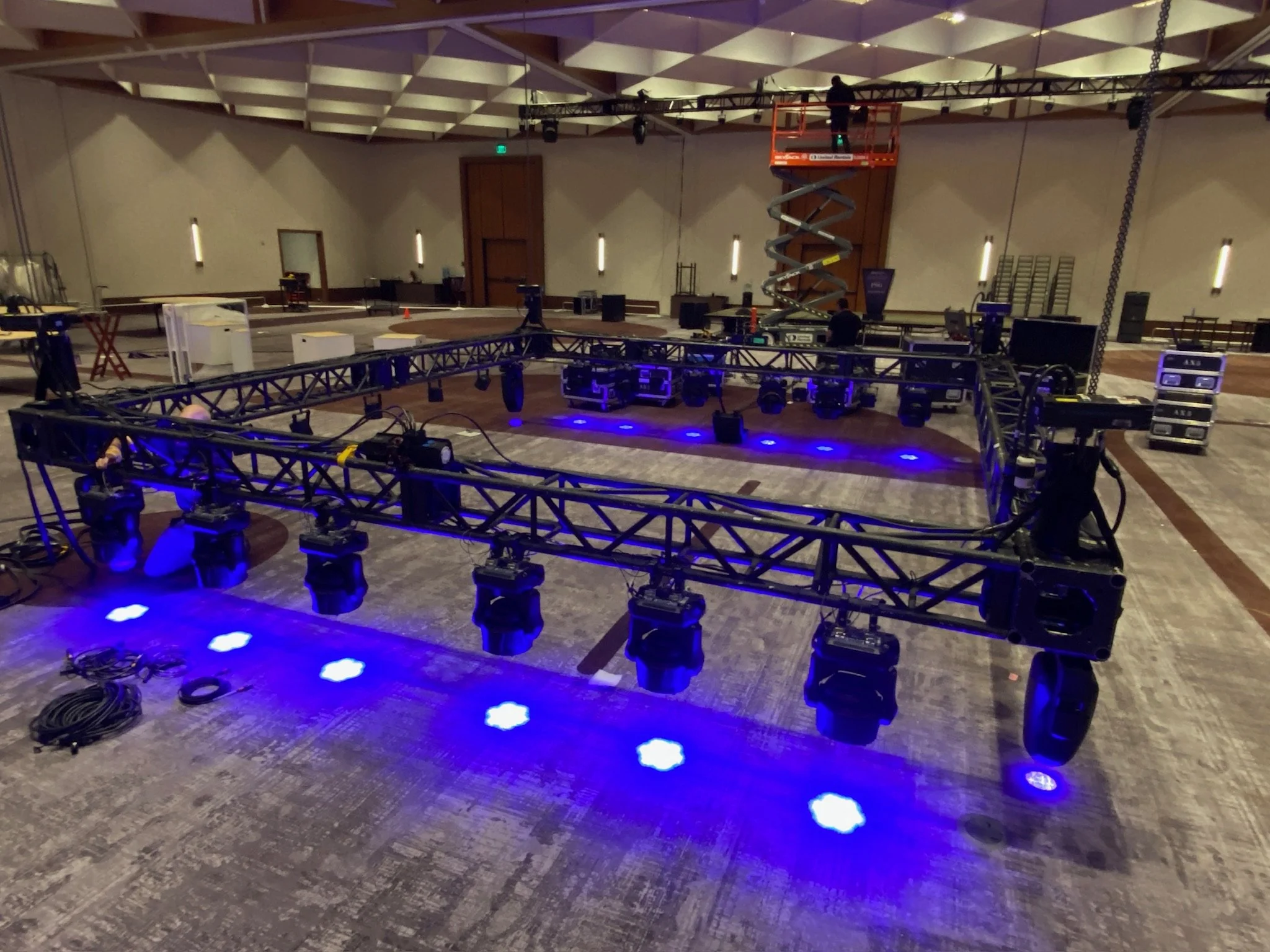 Empty event space with lighting and truss setup, including a scissor lift and stage lights on the floor.