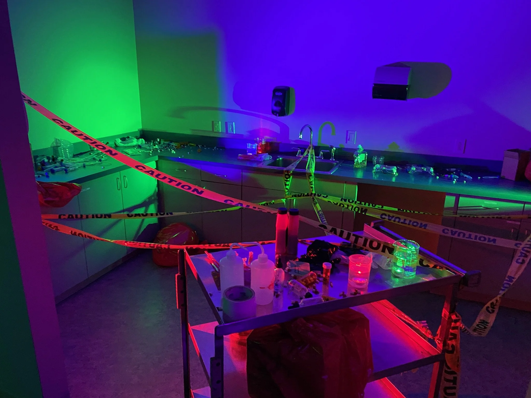 Laboratory with caution tape, illuminated by red, green, and blue lights, containing scientific equipment and chemicals on the tables