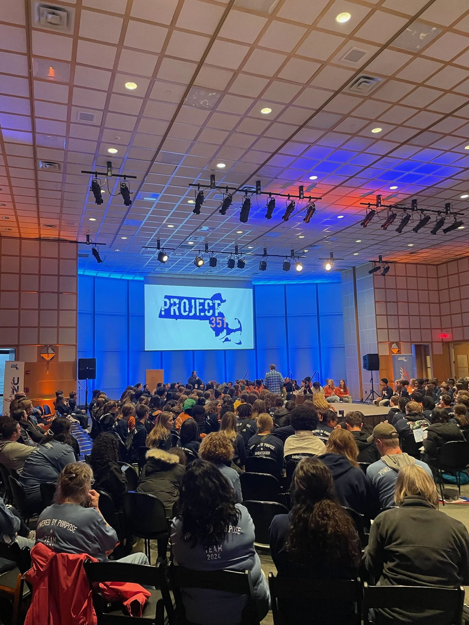 A large indoor conference with many attendees seated facing a stage with a screen displaying the text 'PROJECT 351' and an outline of the state of Illinois with a lion. The room has a high ceiling with stage lighting.