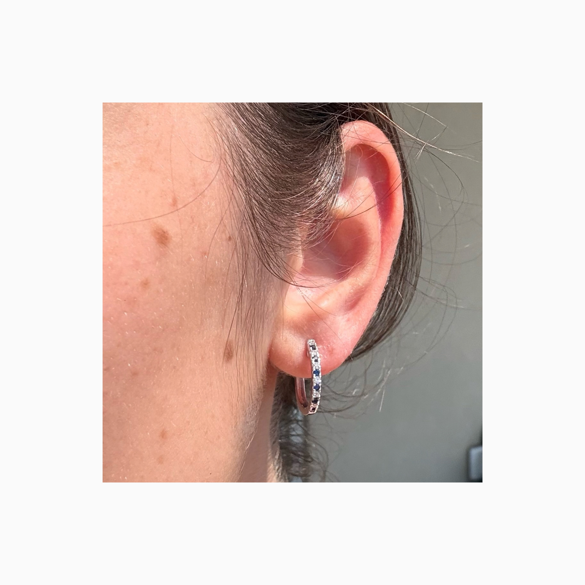 Blue sapphire and diamond huggie earring in 14K white gold shown on ear
