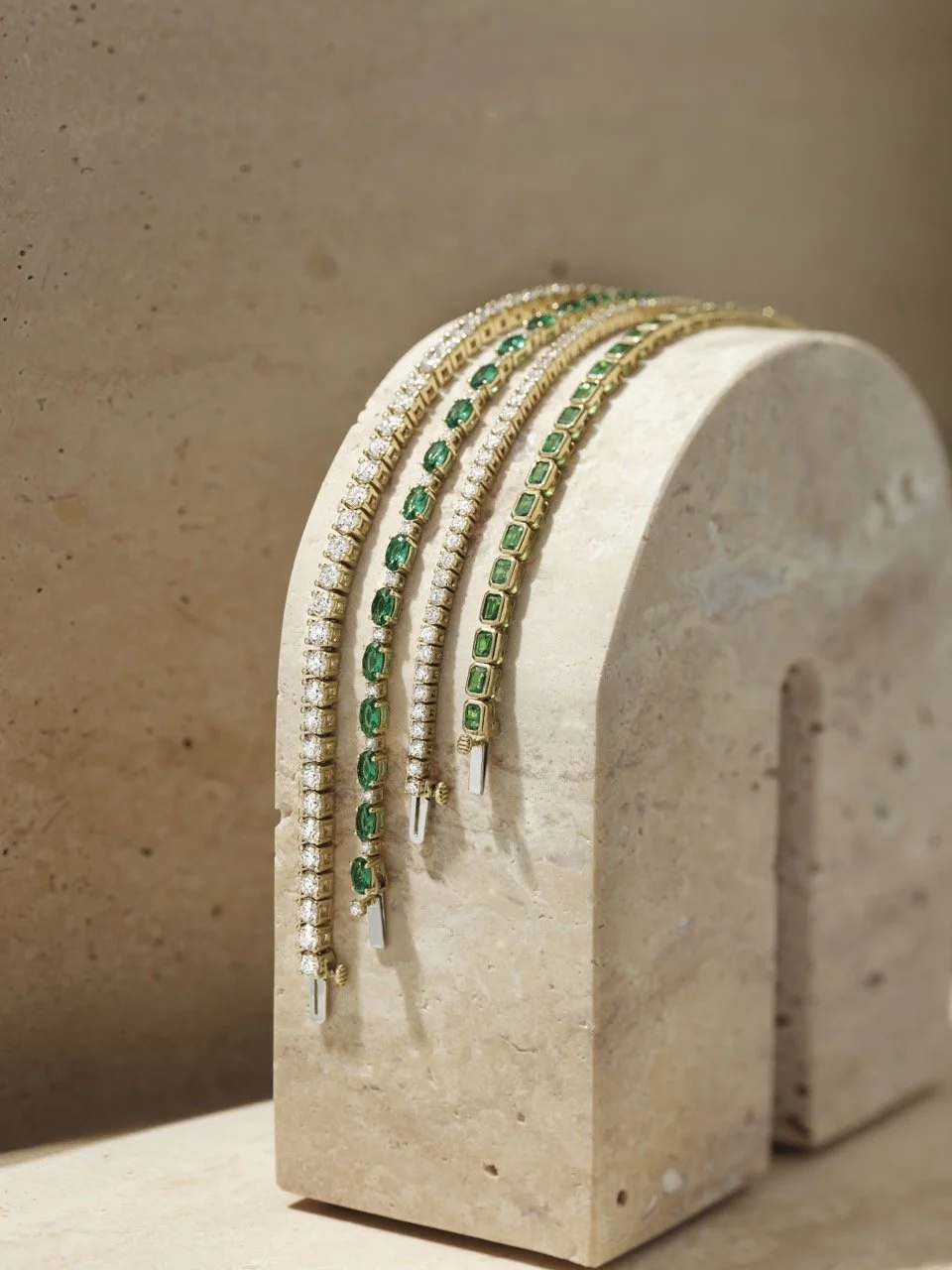 Fine gold bracelets with diamonds, emeralds, and tsavorite garnet displayed on a stone stand, representing curated everyday luxury jewelry