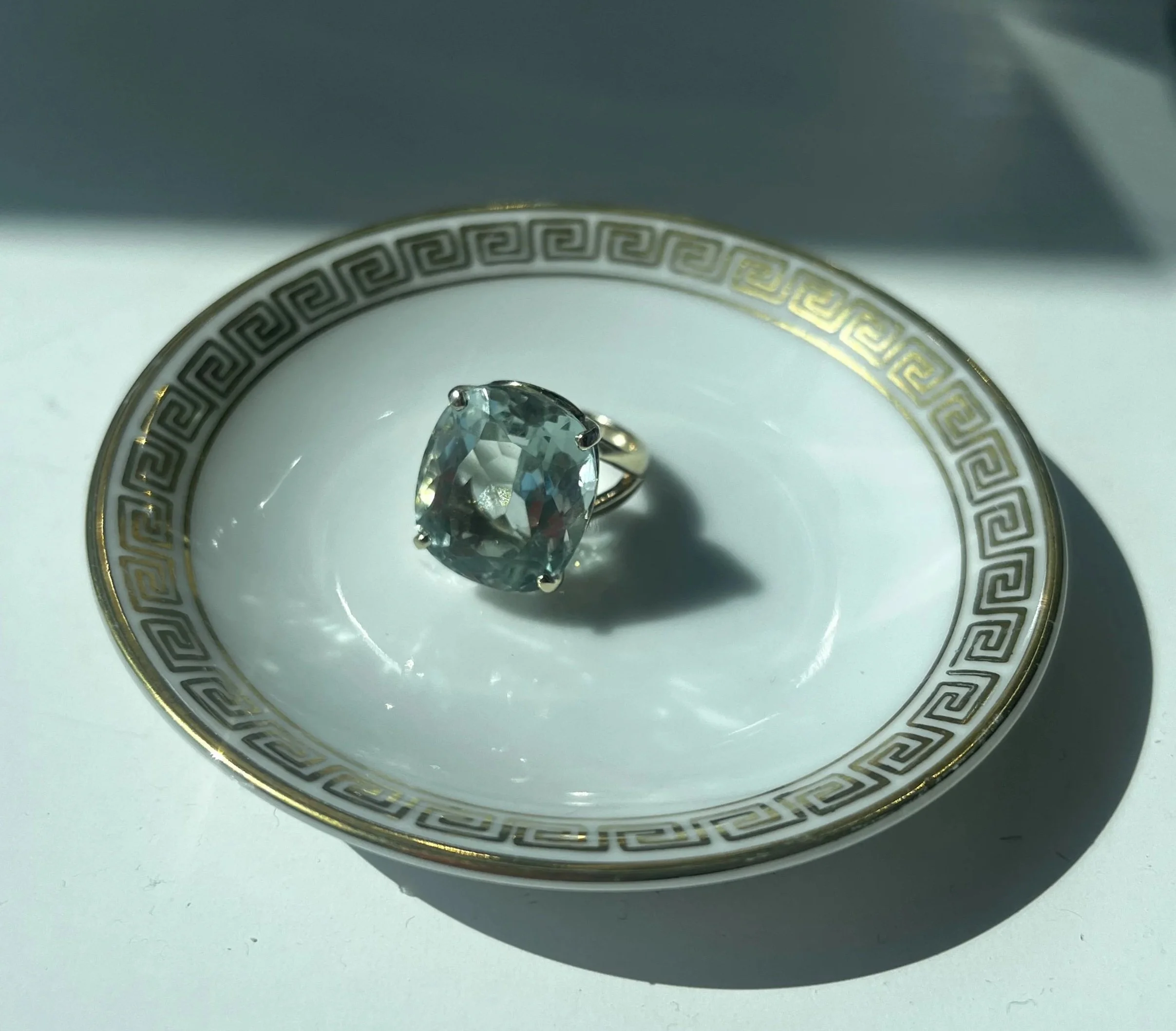 Vintage aquamarine ring in gold setting displayed on white porcelain plate with gold detailing