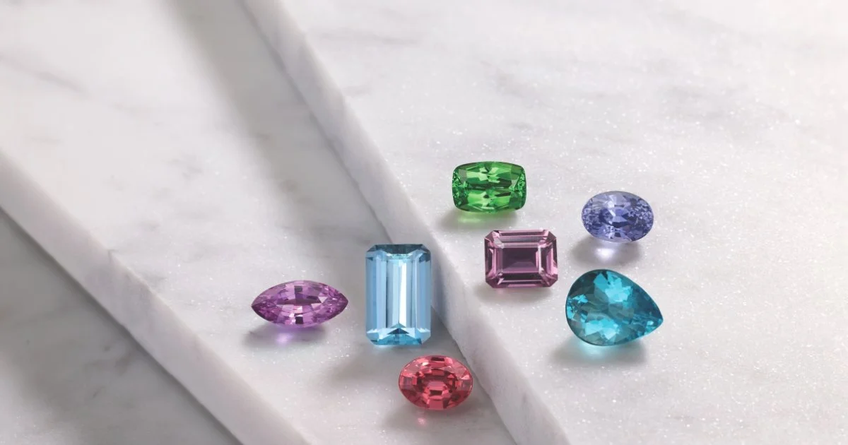 Assorted colorful gemstones including sapphire, spinel, garnet, and aquamarine displayed on white marble background
