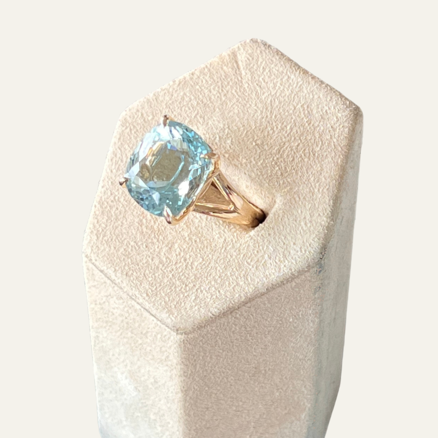 Natural elongated cushion cut aquamarine and gold ring , displayed on a white jewelry stand.