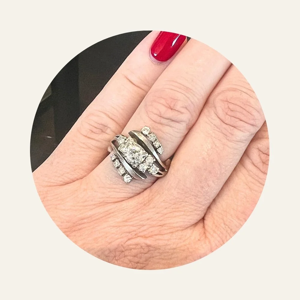 Close-up of a hand with platinum ring featuring natural diamonds on the ring finger, red painted fingernails, and visible skin texture.