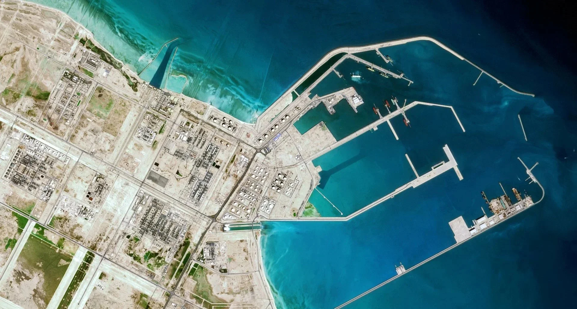Satellite view of a commercial port with docks, ships, breakwaters, and surrounding infrastructure.