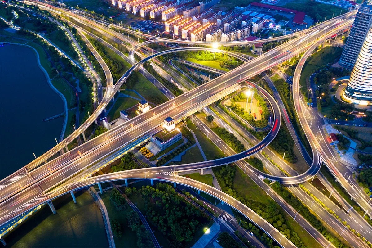 Aerial view of a complex highway interchange with multiple overpasses and ramps illuminated with streetlights in a city at night.