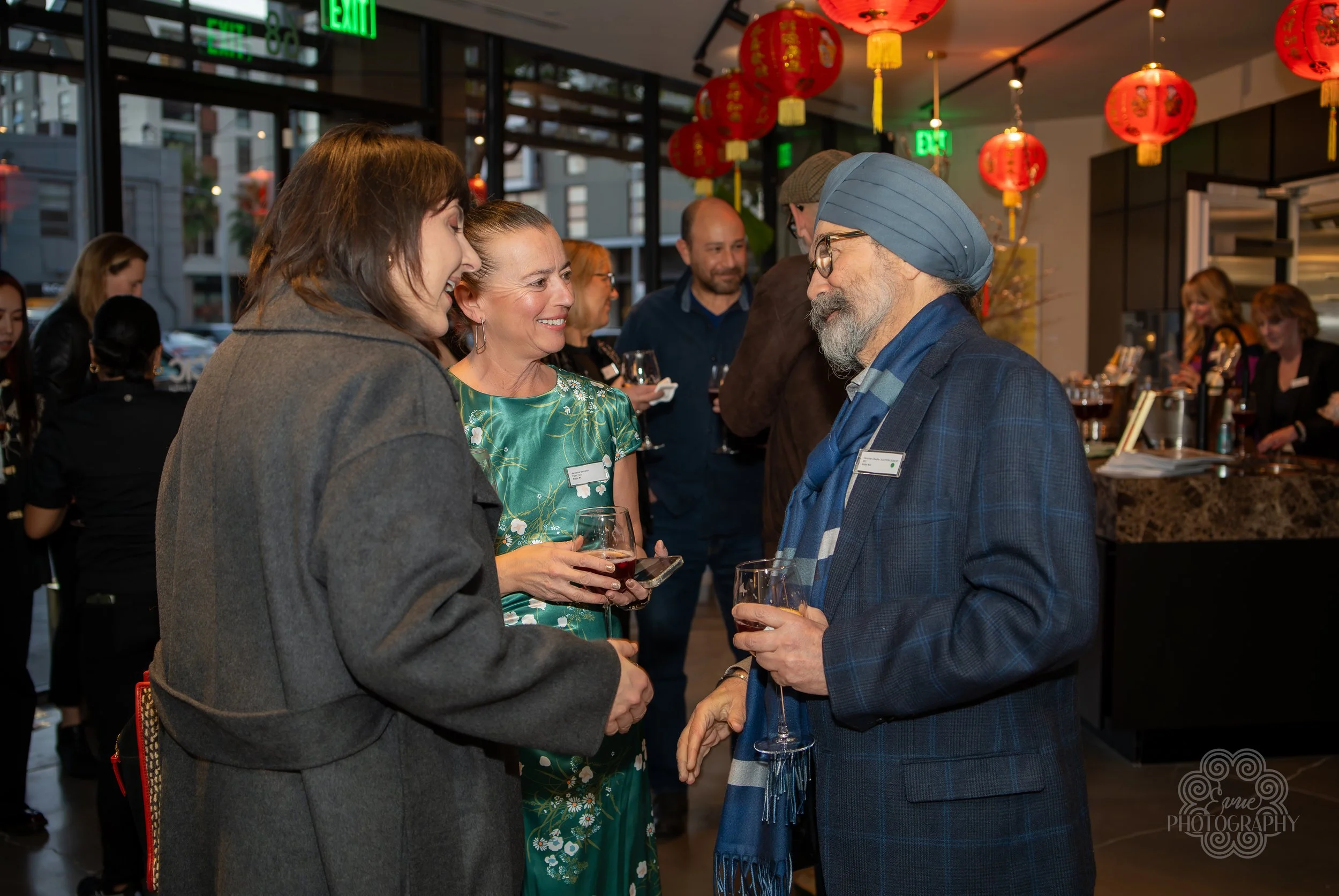 People socializing at a party with red paper lanterns and a bar in the background.