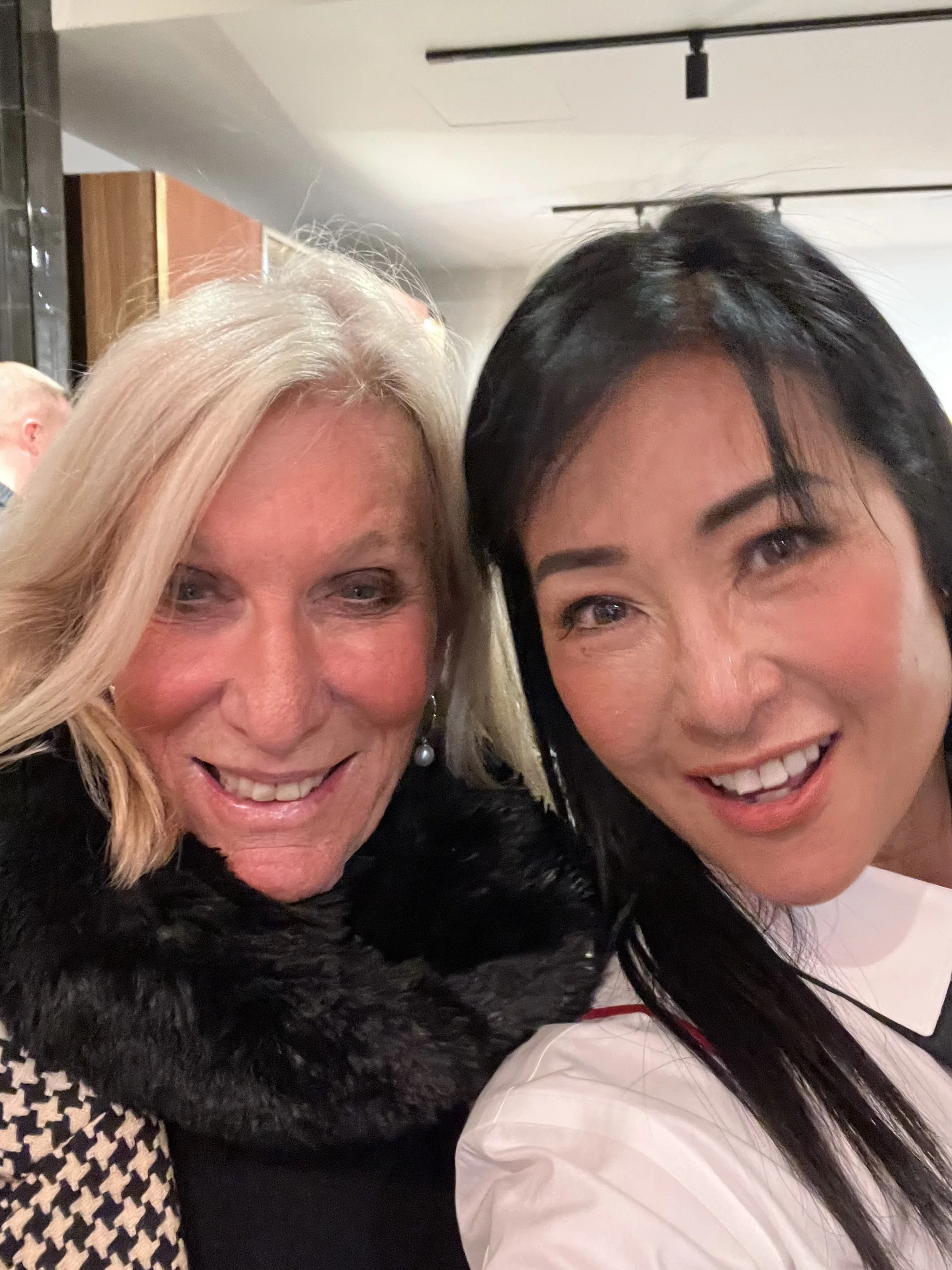 Two women smiling and taking a selfie together indoors.