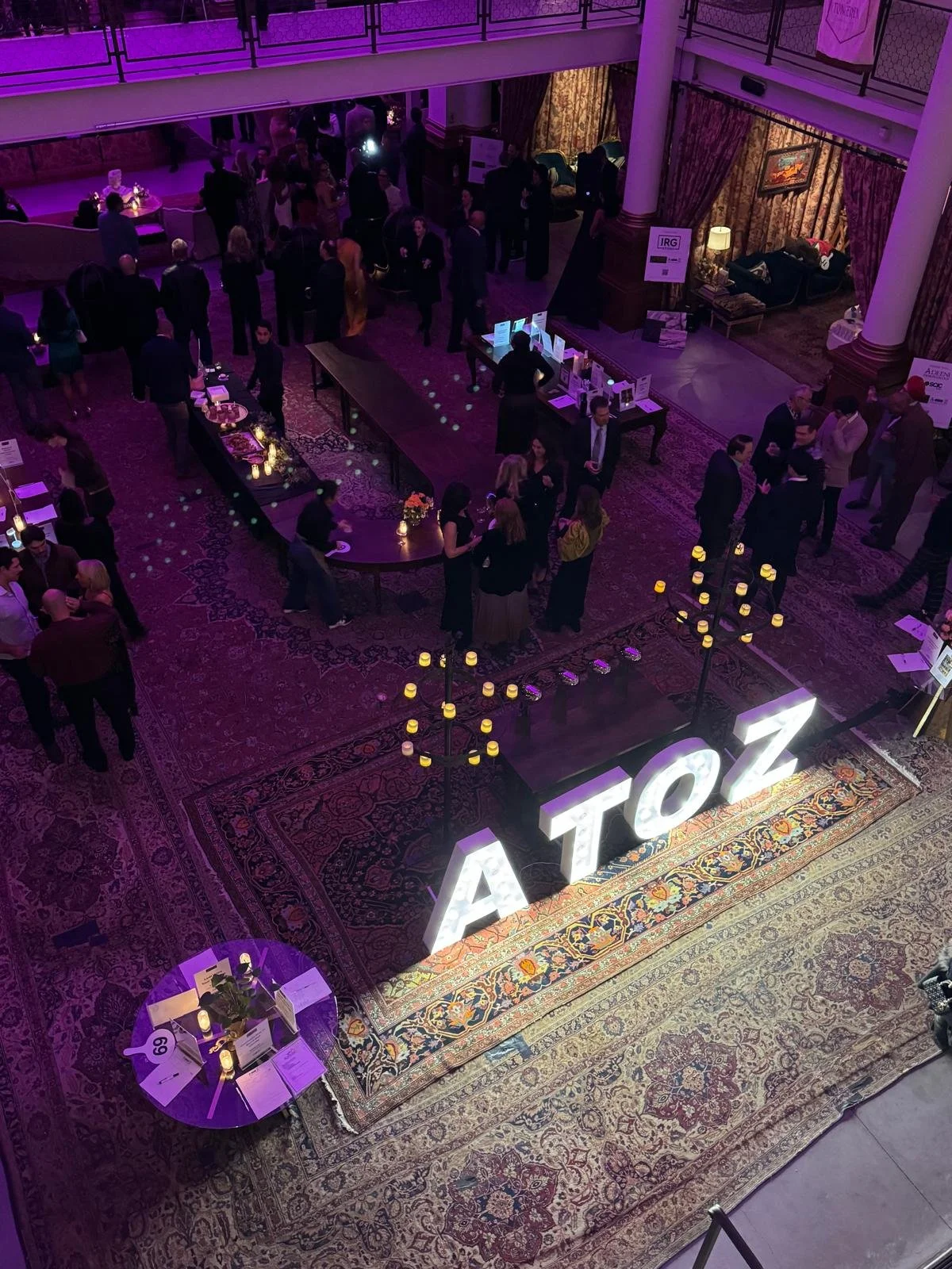 An indoor event with people mingling around tables and a large illuminated sign that says 'AToZ' on a carpeted floor.