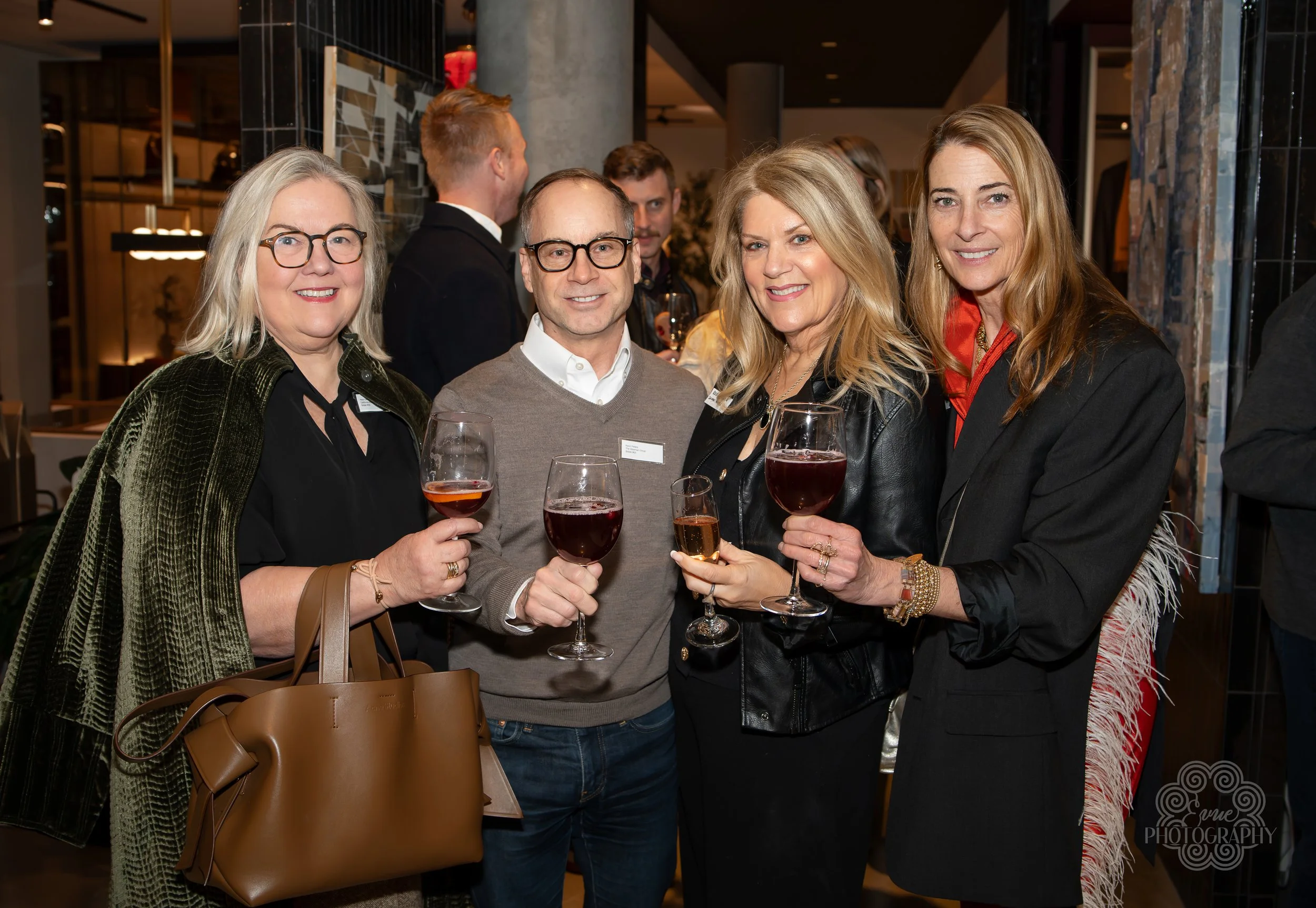 Four adults at a social gathering holding glasses of red wine, smiling at the camera, indoors with modern decor.