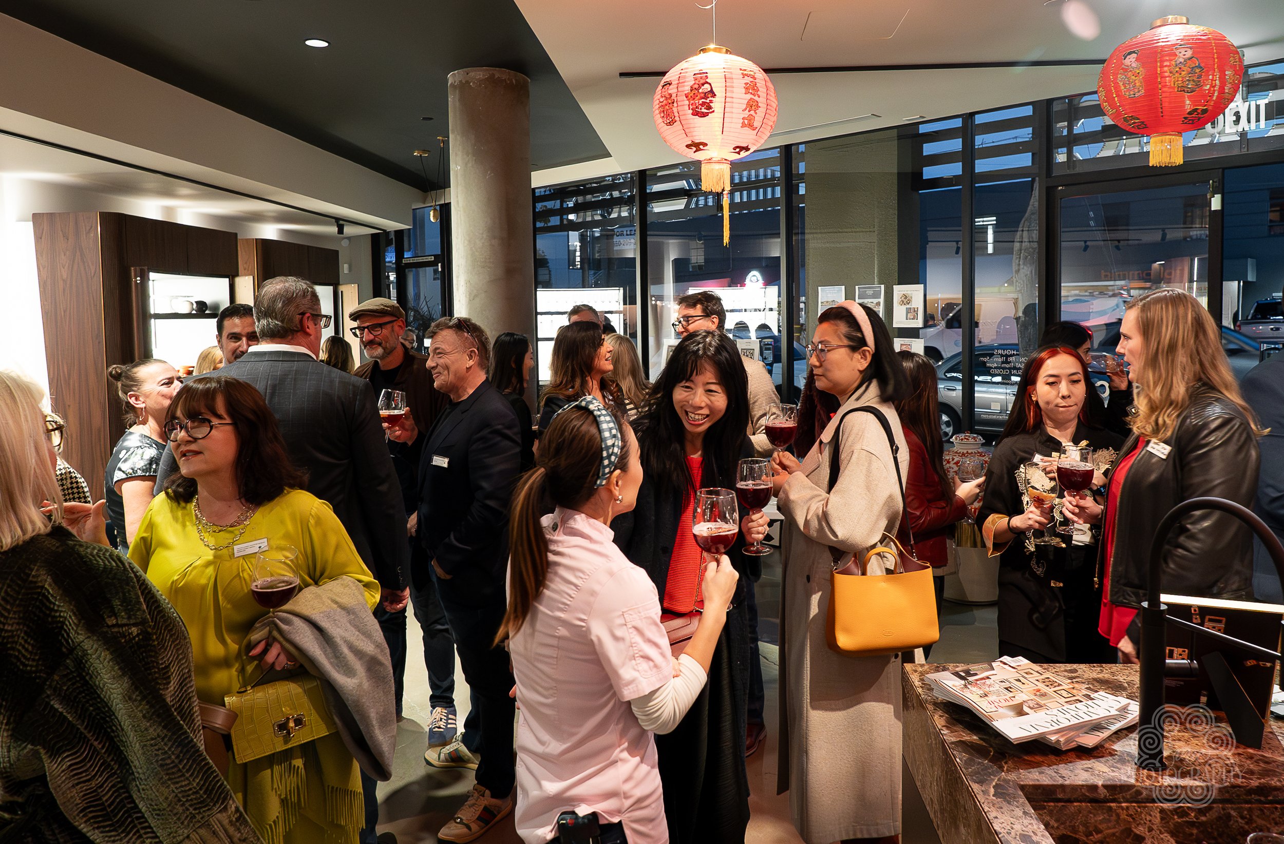 People socializing at an evening event inside a restaurant with Asian-themed red lanterns hanging from the ceiling and large windows in the background.