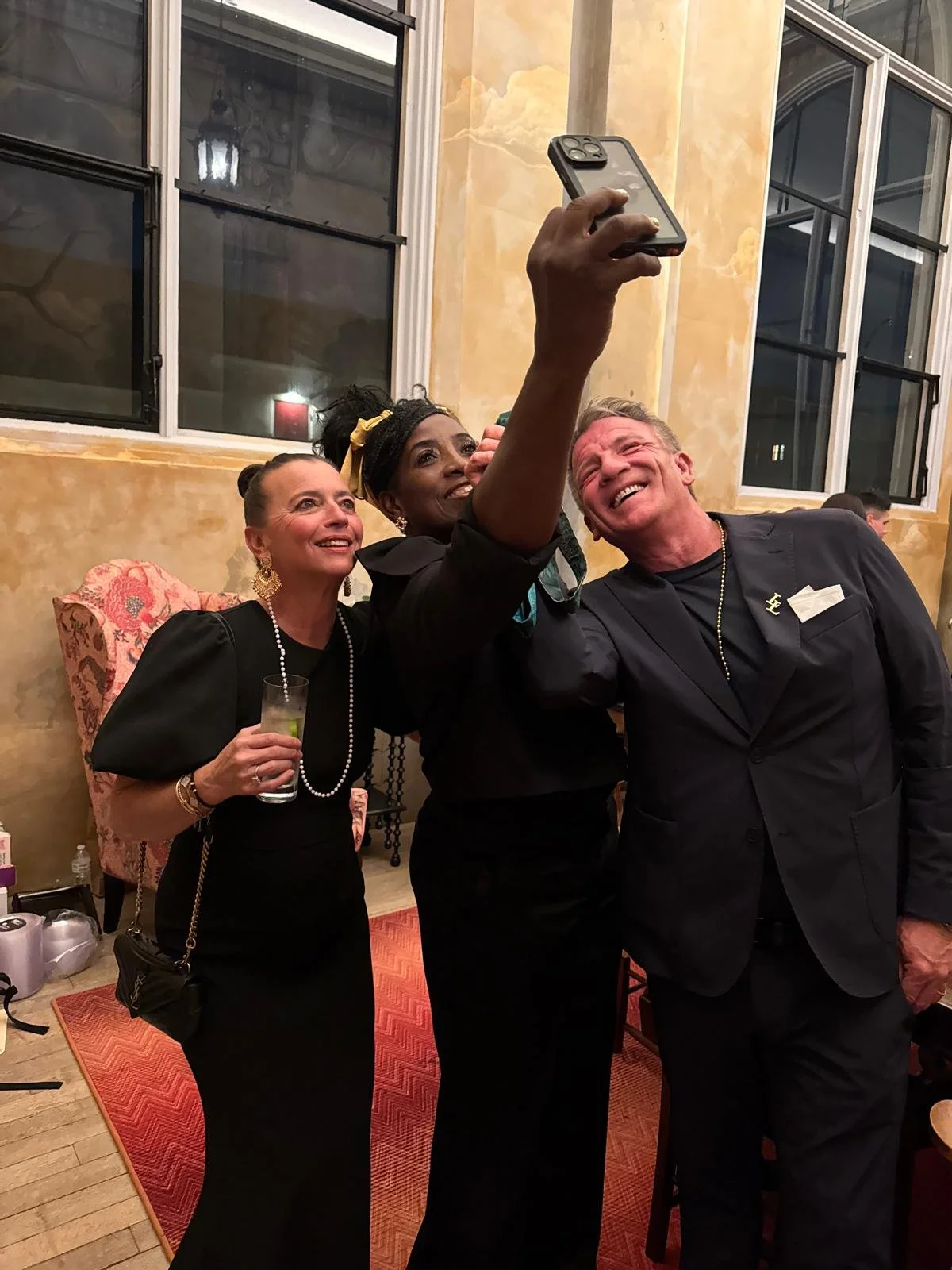 Three people taking a selfie together at a formal event, all smiling, with one person holding a smartphone.