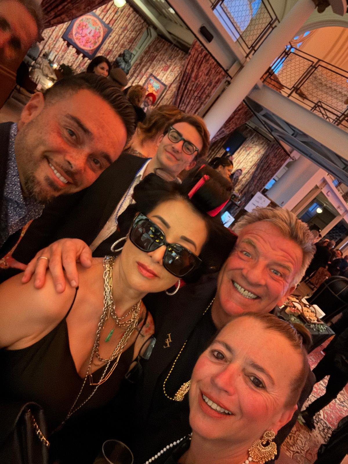 A group of six people at a social event or party, smiling and posing for a selfie indoors.