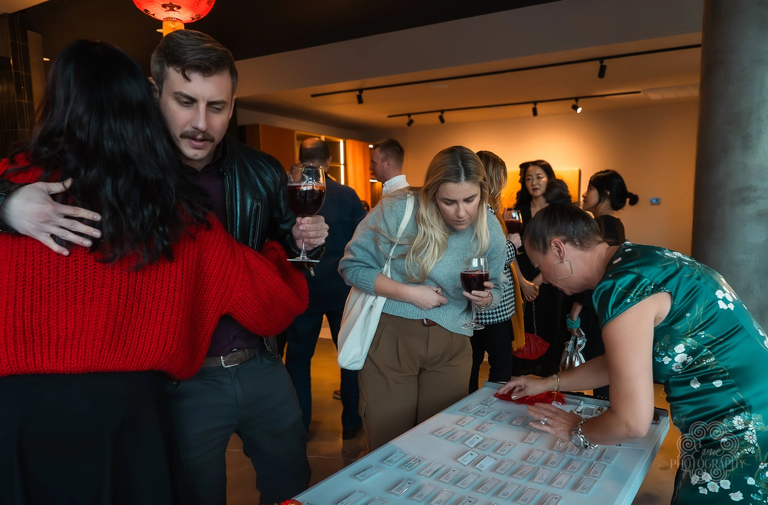 People at a registration table at a social event, with several holding glasses of red wine.