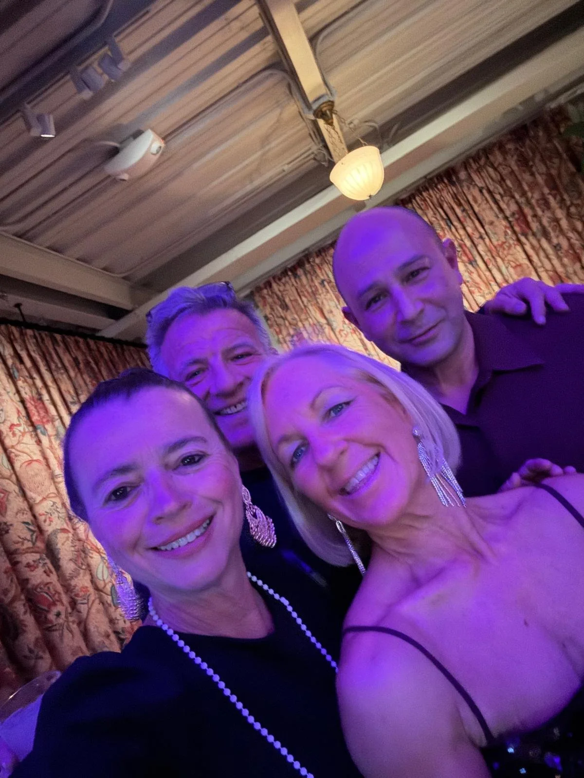 A group of four women and two men taking a selfie at a social gathering with purple lighting.