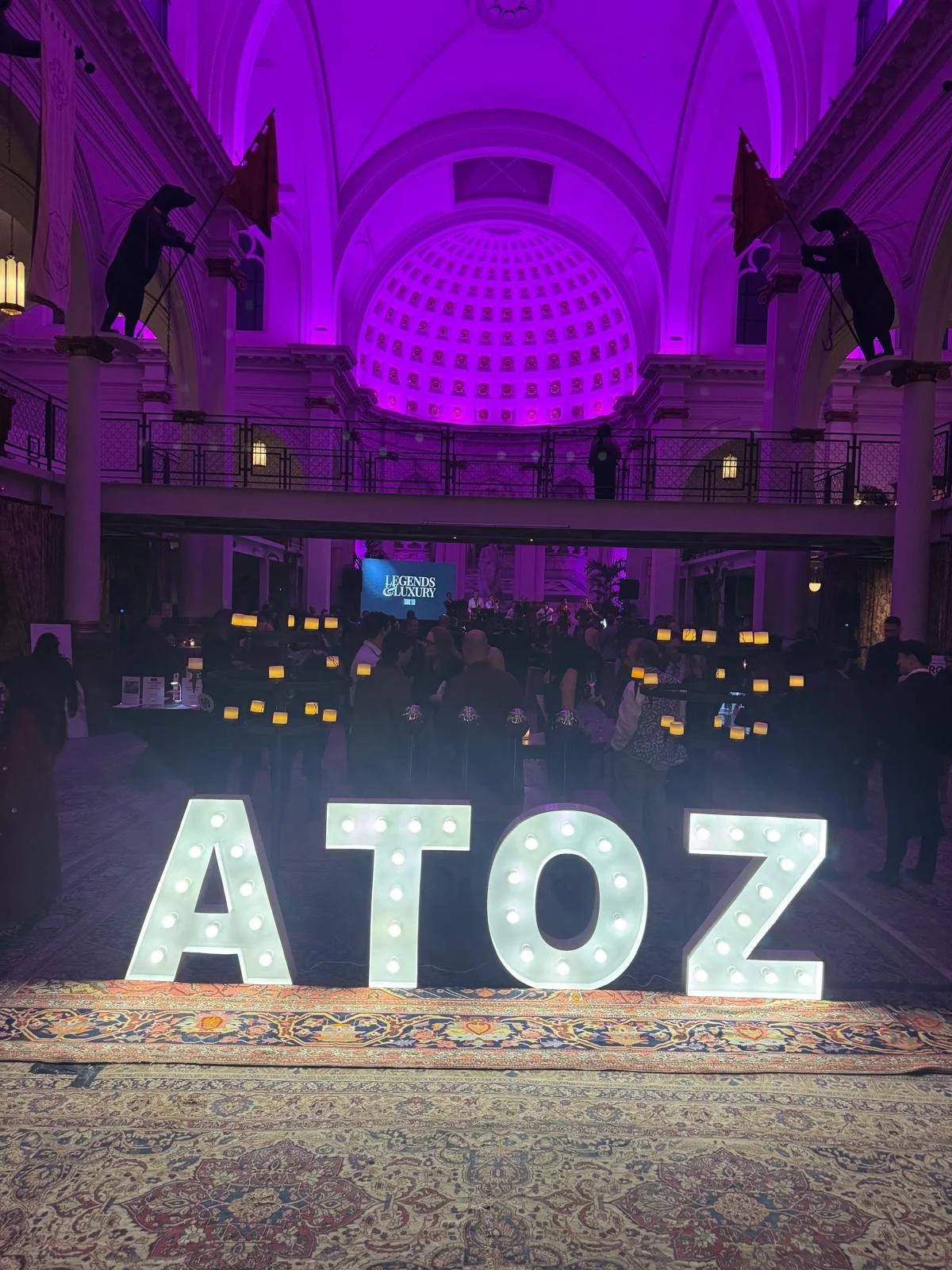Large illuminated sign spelling ATOZ at a formal event in a grand hall with purple lighting, with people mingling and a stage in the background.