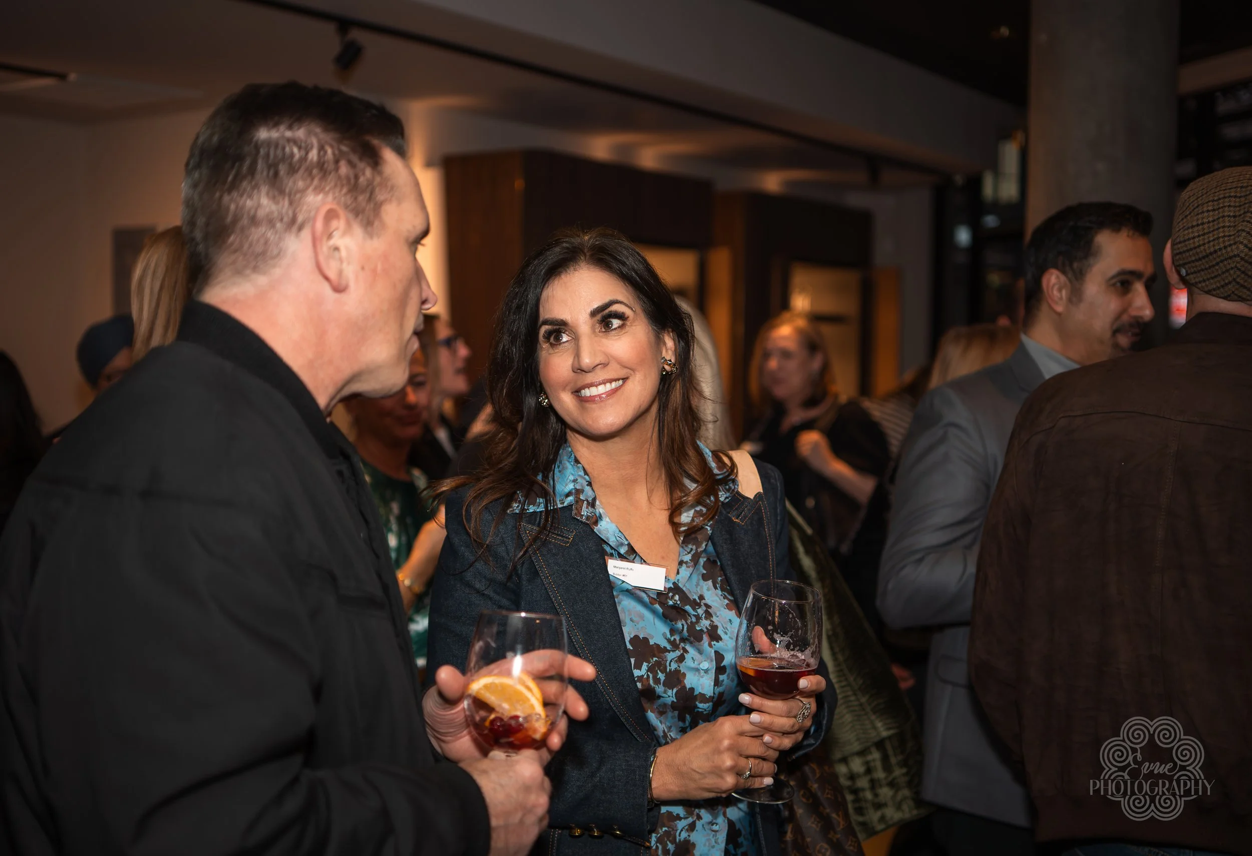 Women and men in a social gathering holding glasses of wine and engaging in conversation.