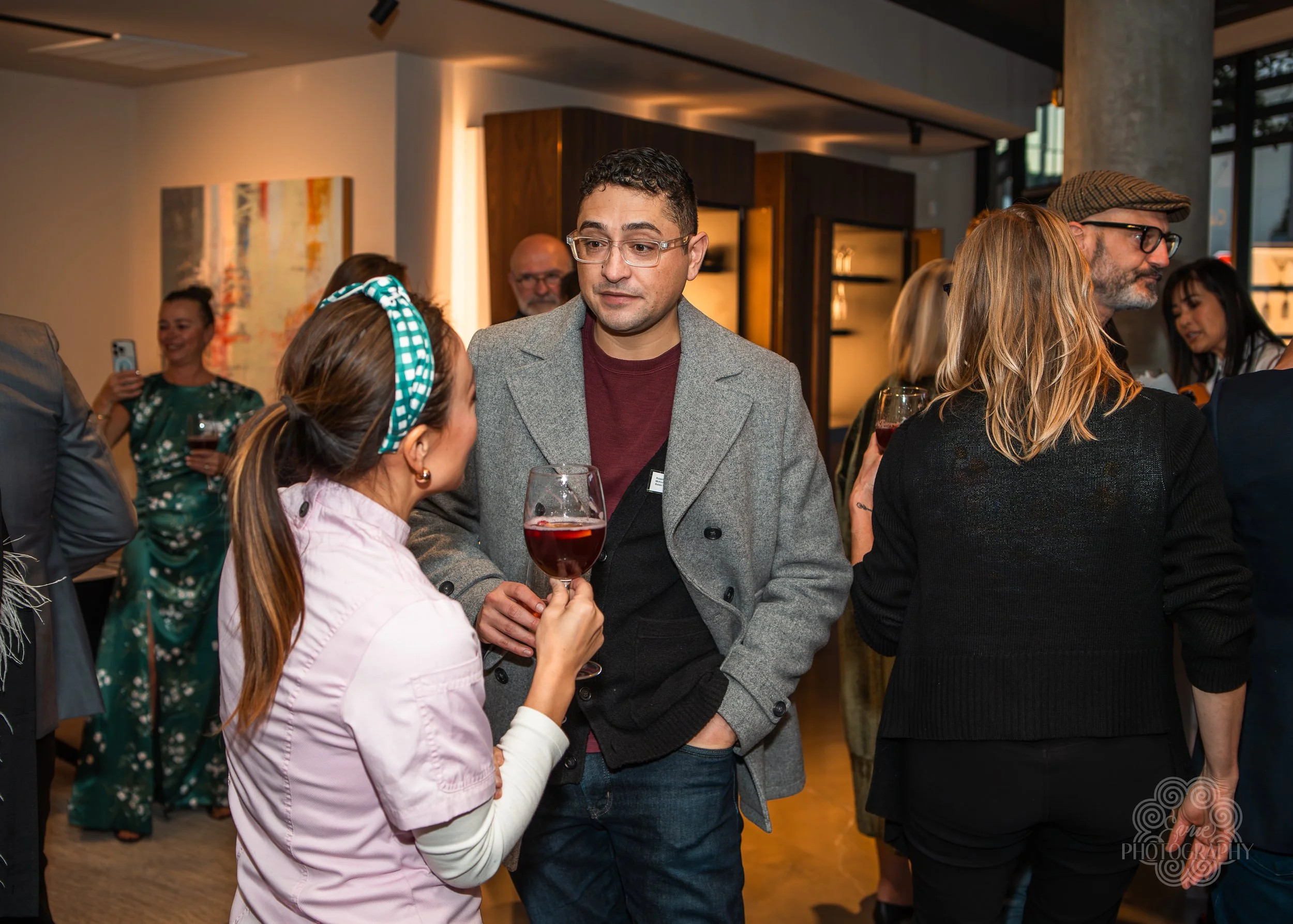 People socializing at an indoor event, some holding glasses of red wine, engaging in conversation.