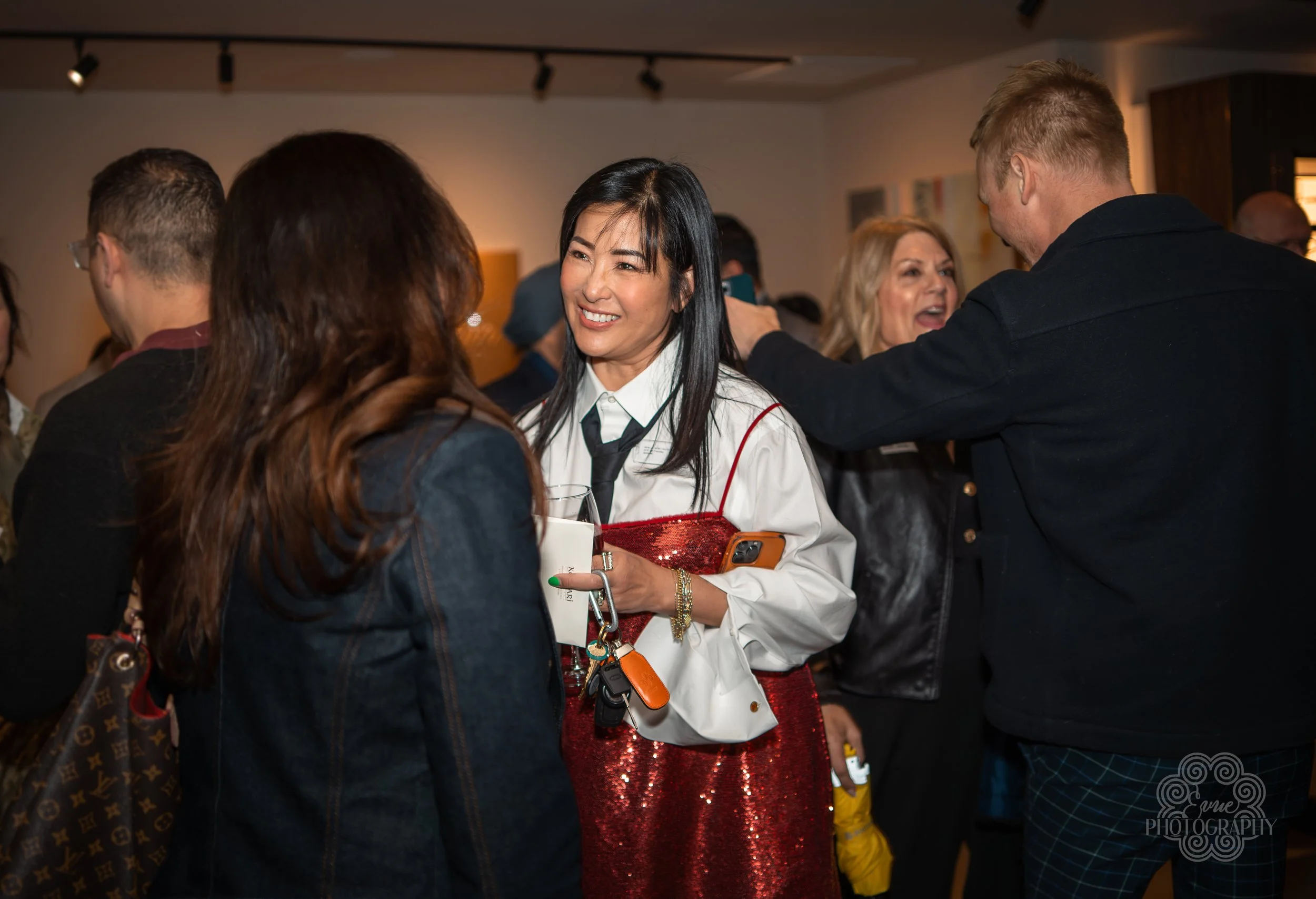 People socializing at an indoor event, engaged in conversation, with some holding drinks.