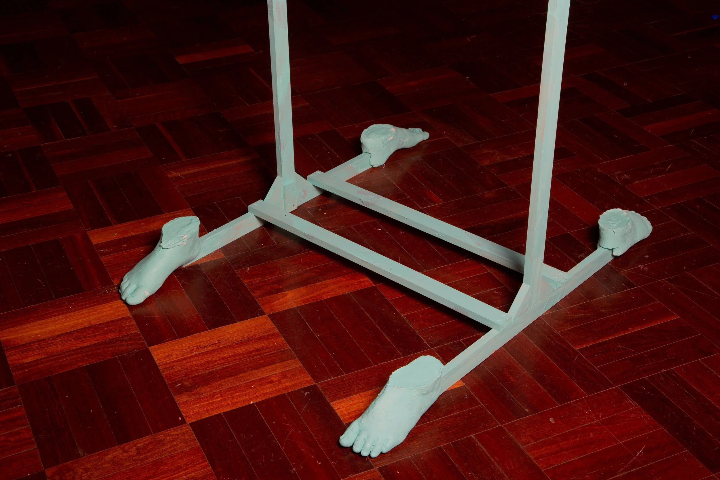 Part of a metal furniture frame with four feet painted light blue on a wooden floor, with some paint chips and imperfections visible.