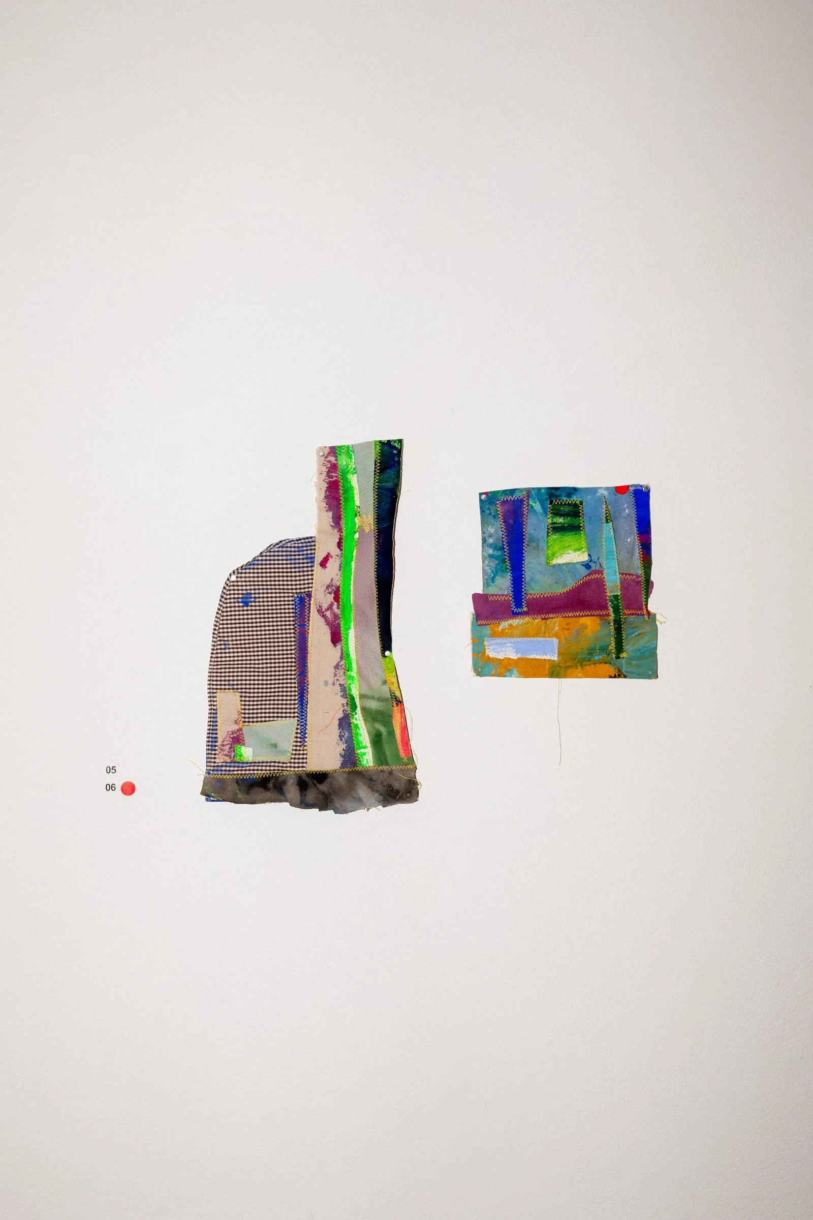 Two colorful textile artworks displayed on a white gallery wall, with small labels underneath.