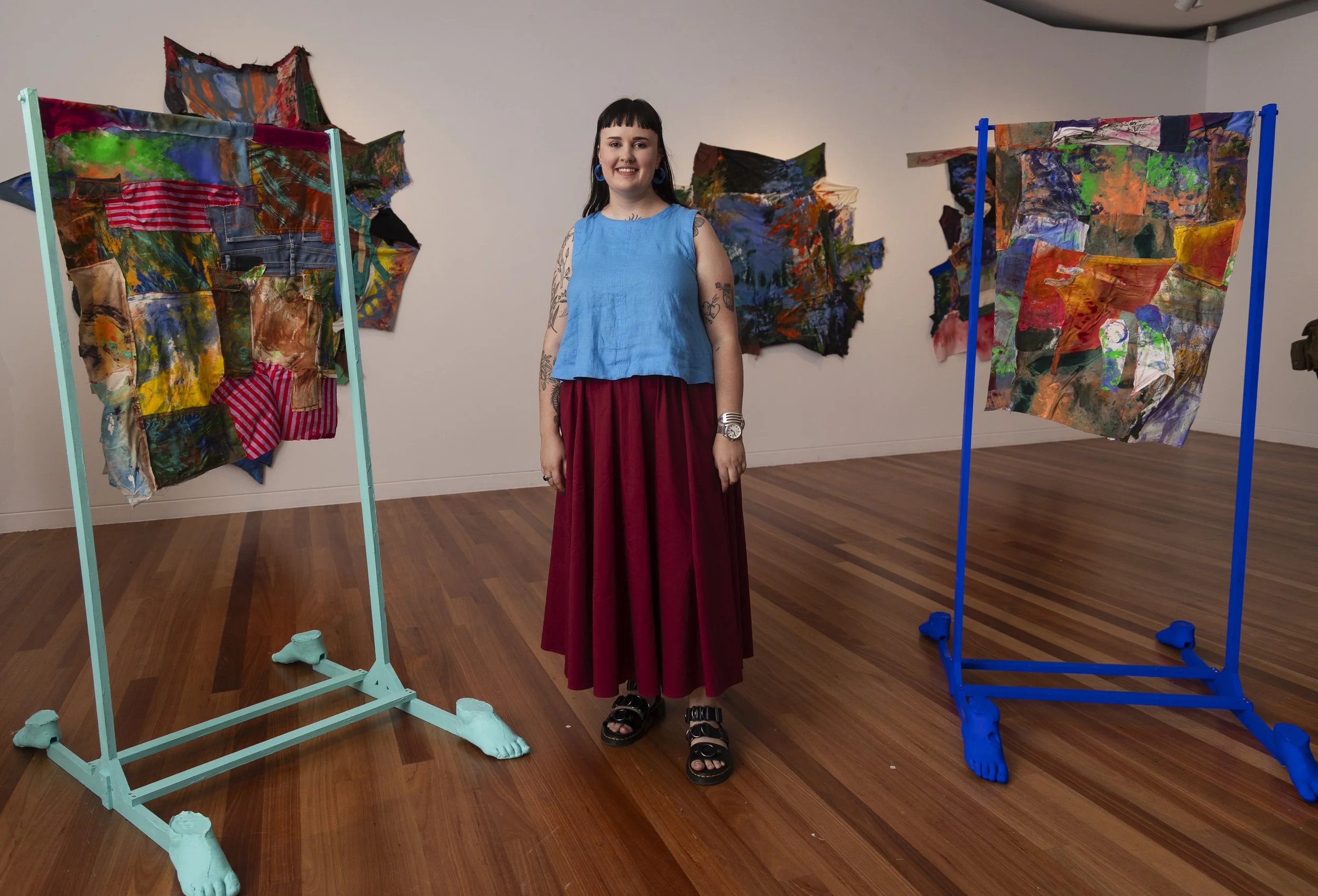 A woman standing in an art gallery with colorful abstract fabric art pieces on display on two blue and aqua stands.