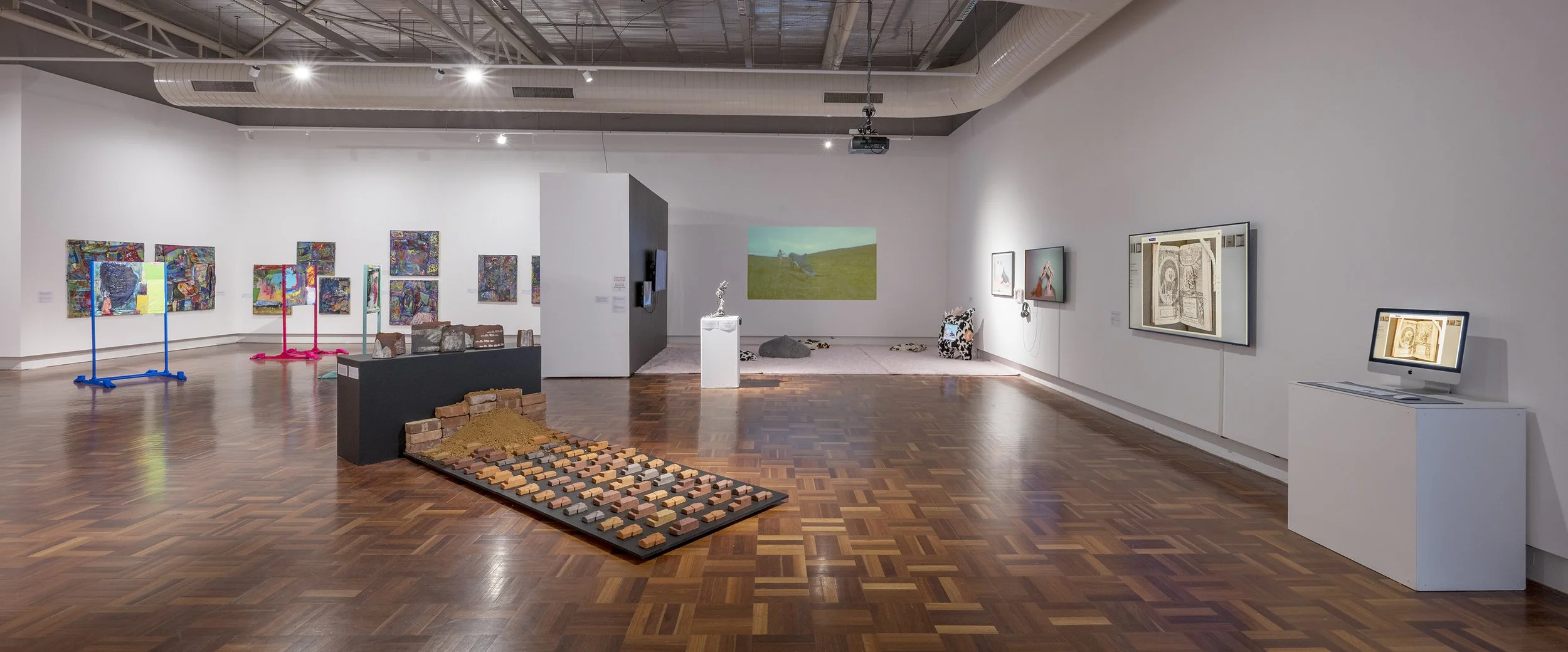 Art gallery with colorful paintings on the walls, sculptures, digital screens, and multimedia art installations on a wooden floor.