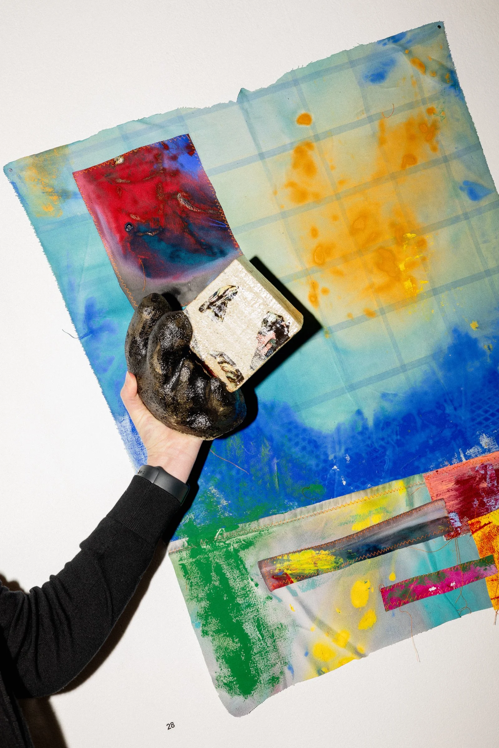 A person holding a leather wallet or small bag, standing in front of a colorful abstract artwork on a white wall.