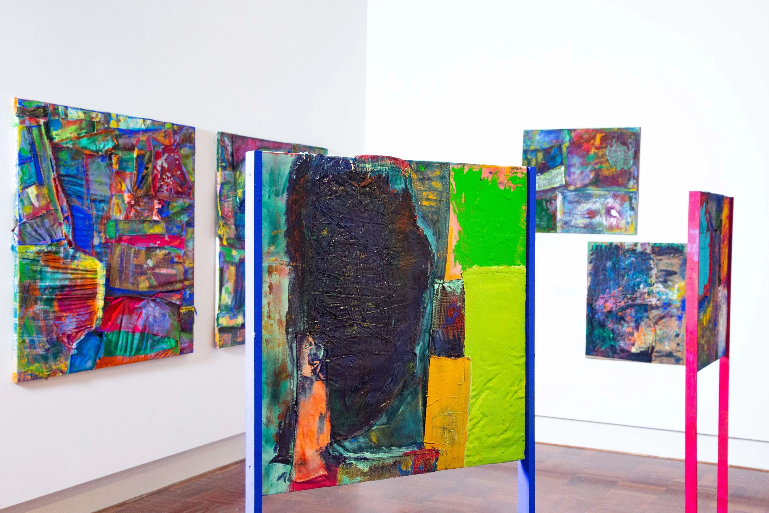 Colorful abstract paintings on display in an art gallery with white walls and wooden floors.
