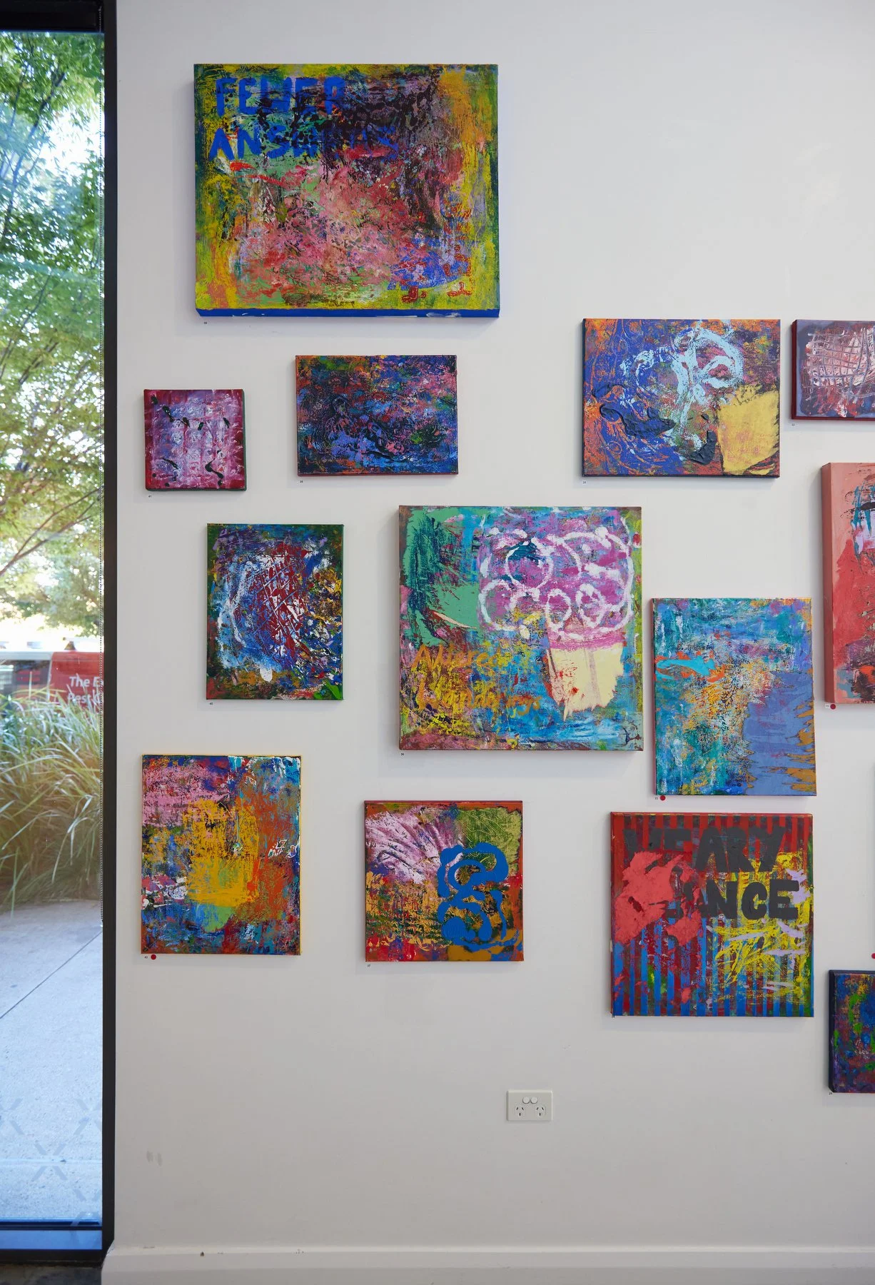 A collection of colorful abstract paintings displayed on a white wall in an art gallery.