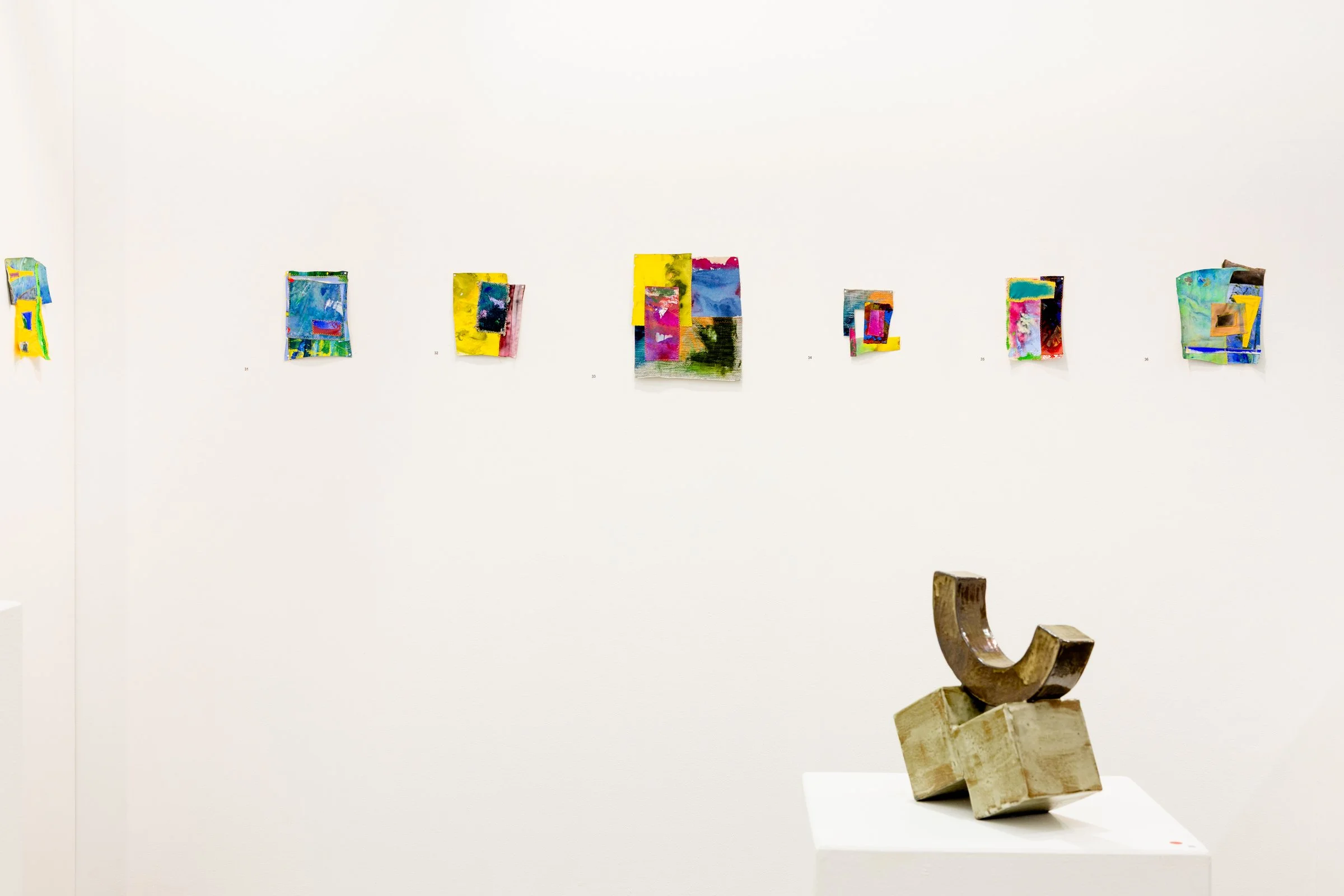 Gallery with colorful abstract paintings on the wall and a beige sculpture on a white pedestal in the foreground.