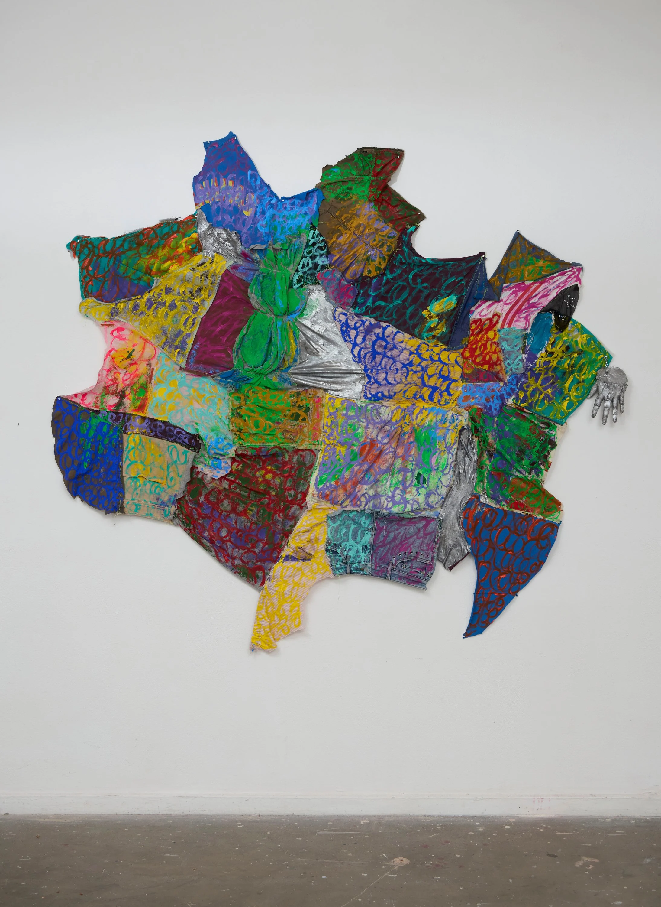 Mixed media art piece of an abstract shape with colorful painted patterned fabrics and metallic elements displayed on a wall.