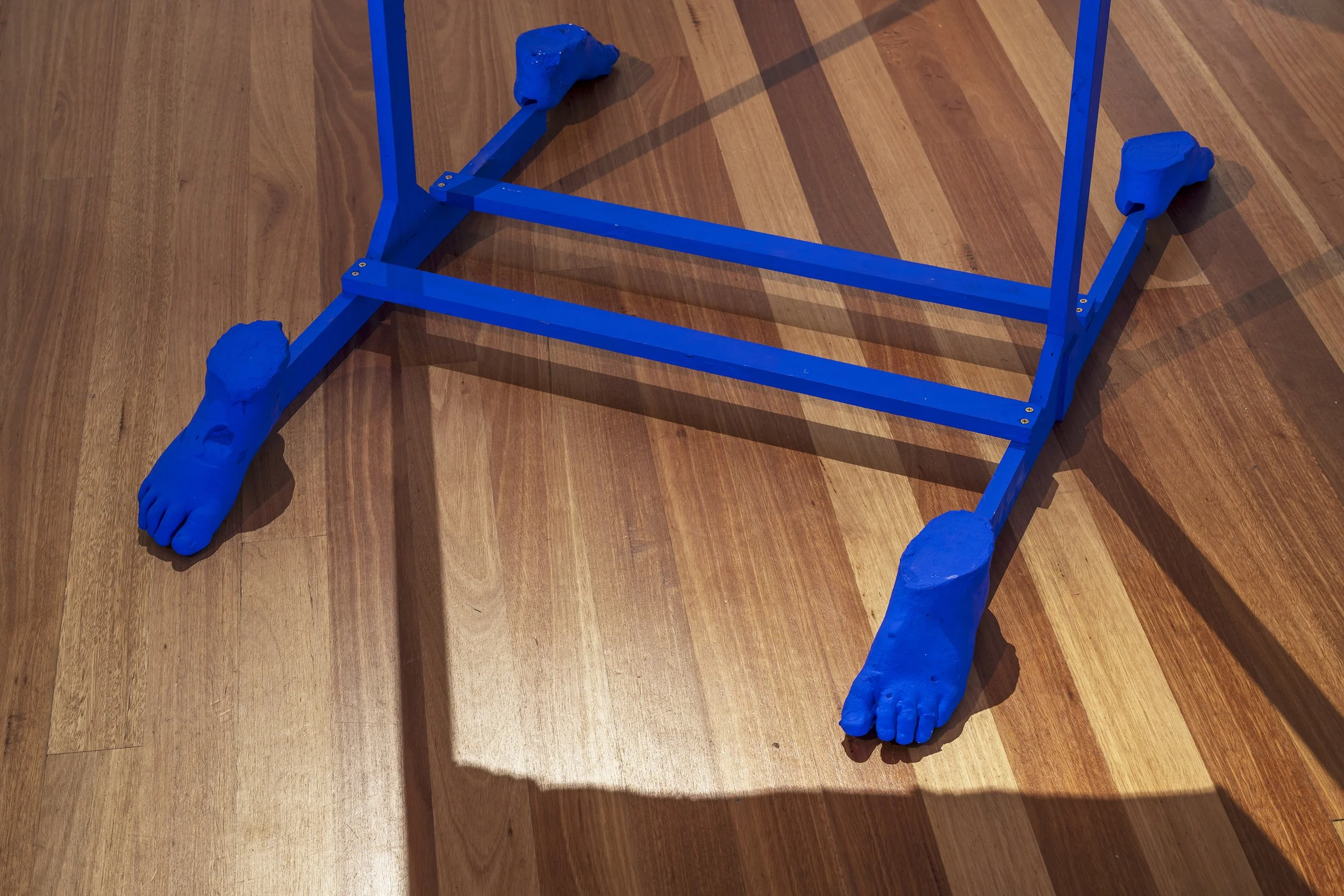 Blue wooden chair with feet and leg sculptures, placed on a hardwood floor.
