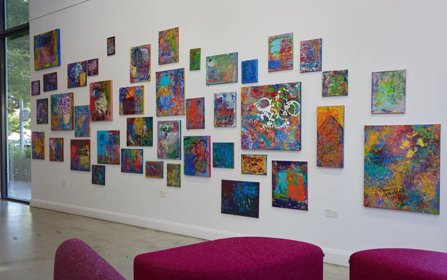 Gallery wall with multiple colorful abstract paintings in a modern art gallery space.