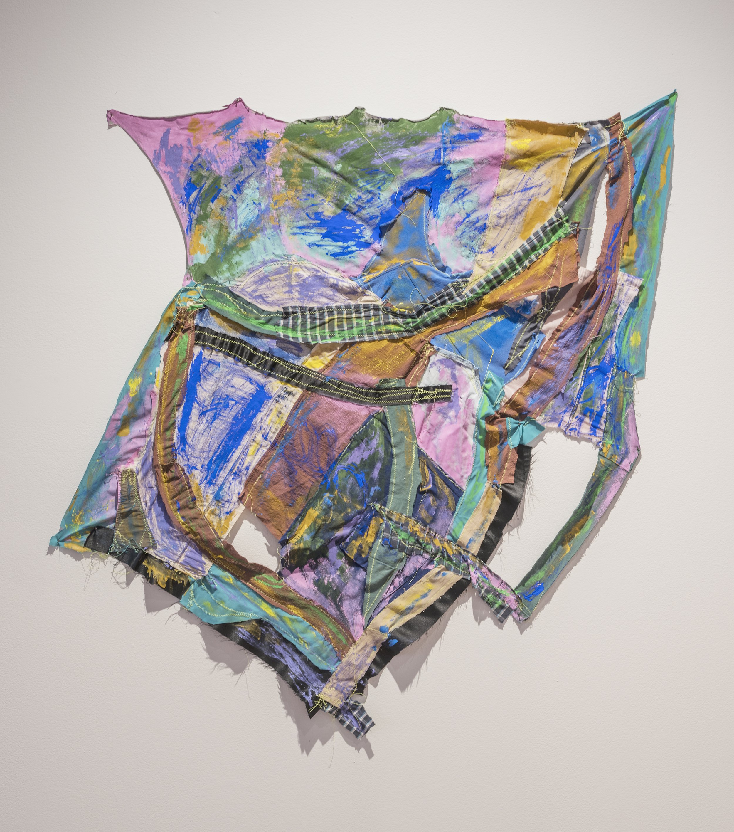 Colorful abstract mixed-media artwork with patches of fabric, painted areas, and visible stitches on a plain white wall.