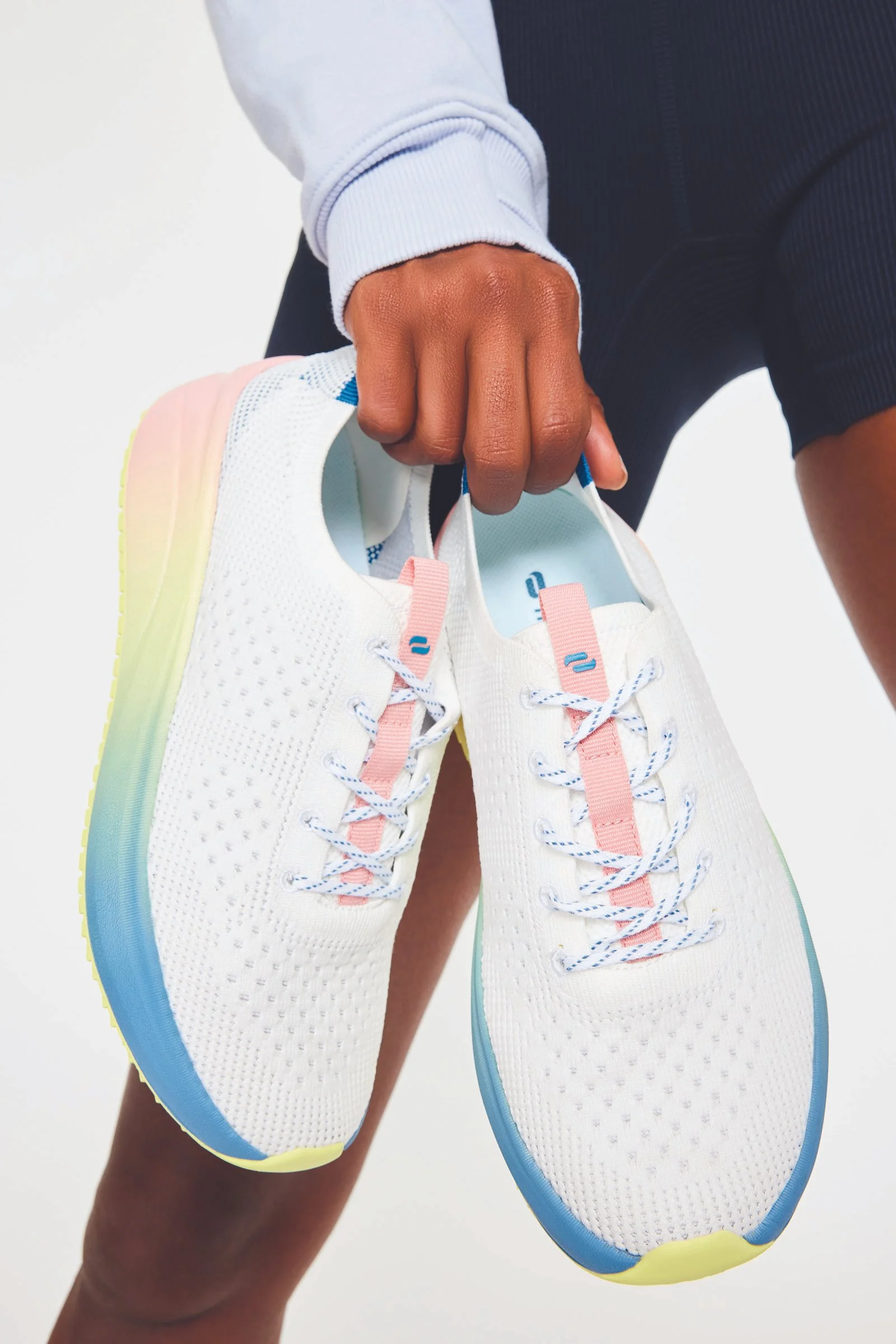 A person holding a pair of white running shoes with pastel-colored midsoles, against a plain background.