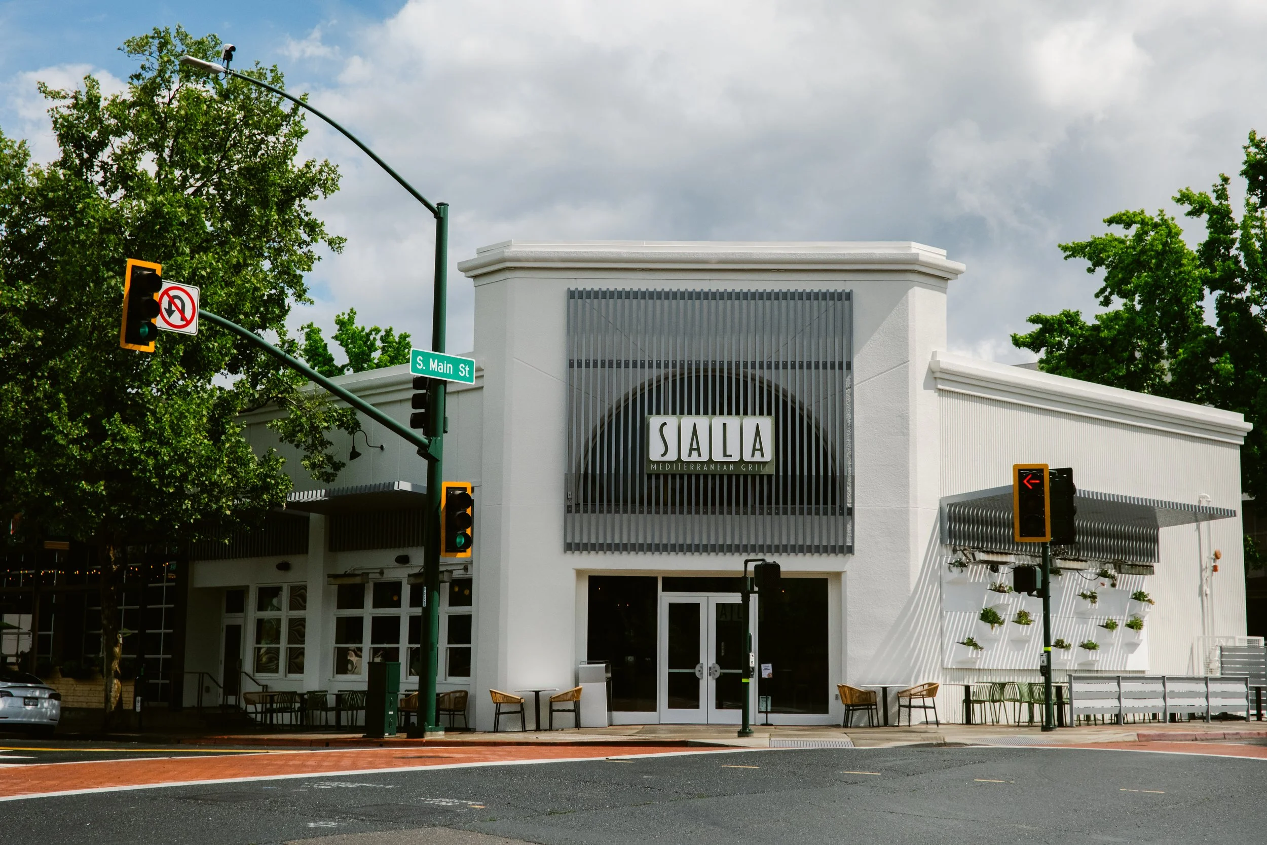 White building with a sign that reads "SALA Mediterranean Grill" on the front, with trees and traffic lights at an intersection on S. Main St.