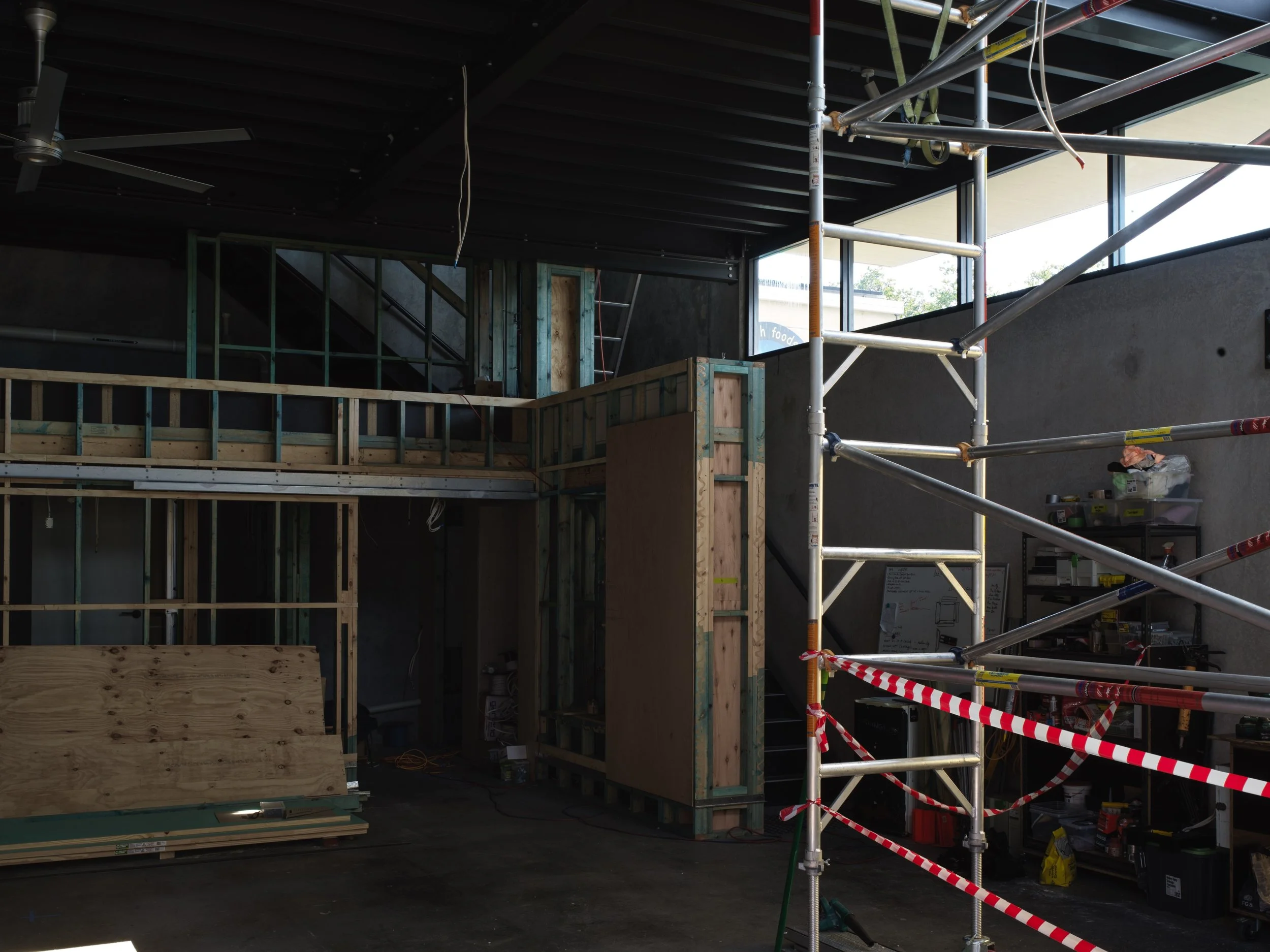 Interior of a building under construction with wooden framing, scaffolding, and construction tools and supplies.