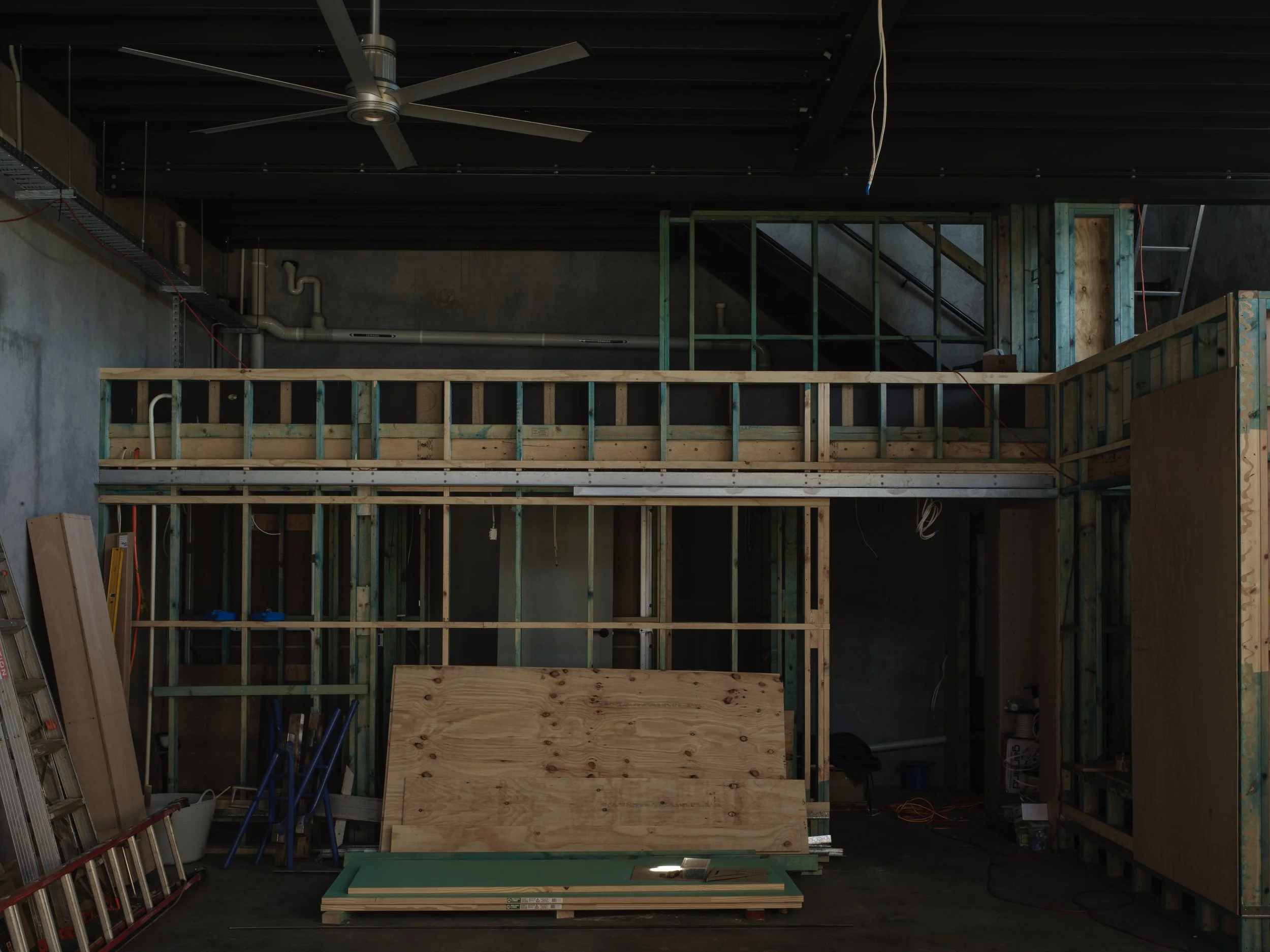 Interior of a building under construction, showing wooden framing, exposed pipes, construction tools, and materials.