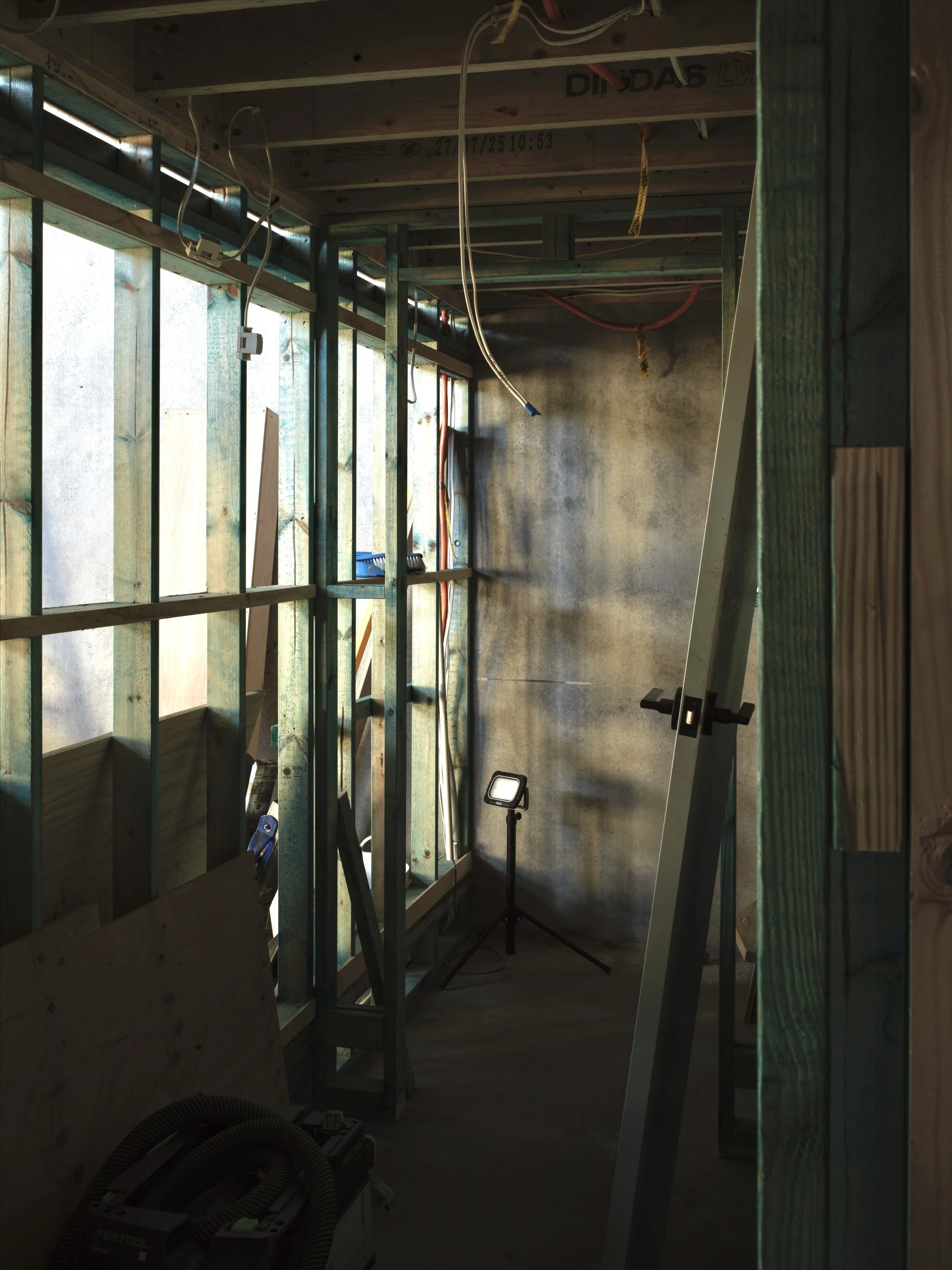 Interior of a building under construction with exposed framing, electrical wiring, and construction tools, including a work light and saw.