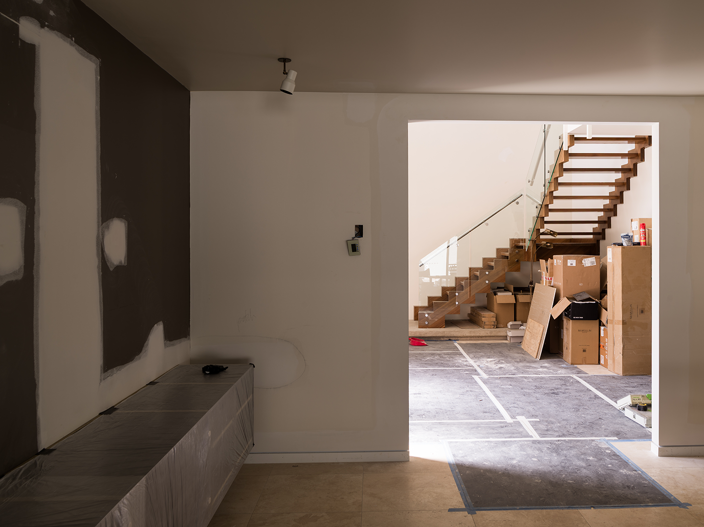 Interior of a house under construction with a wooden staircase, cardboard boxes, and construction materials.