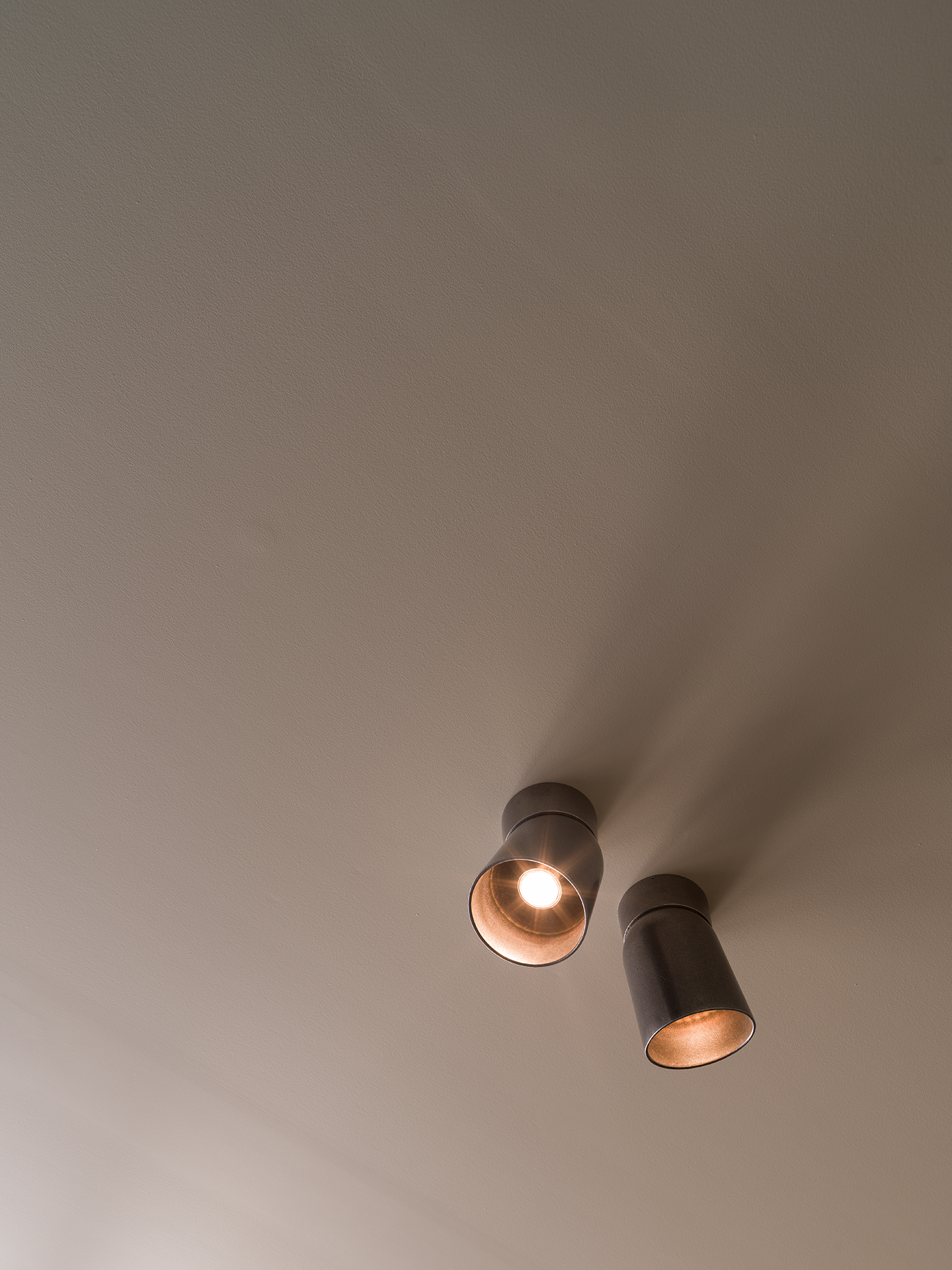 Ceiling spotlight fixture with two cylindrical lights, one turned on, mounted on a beige ceiling.