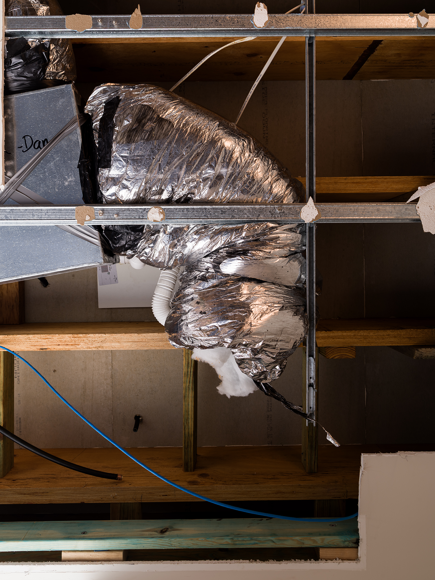 View of an unfinished ceiling with exposed wooden beams, metal shelving, and silver insulated ductwork.