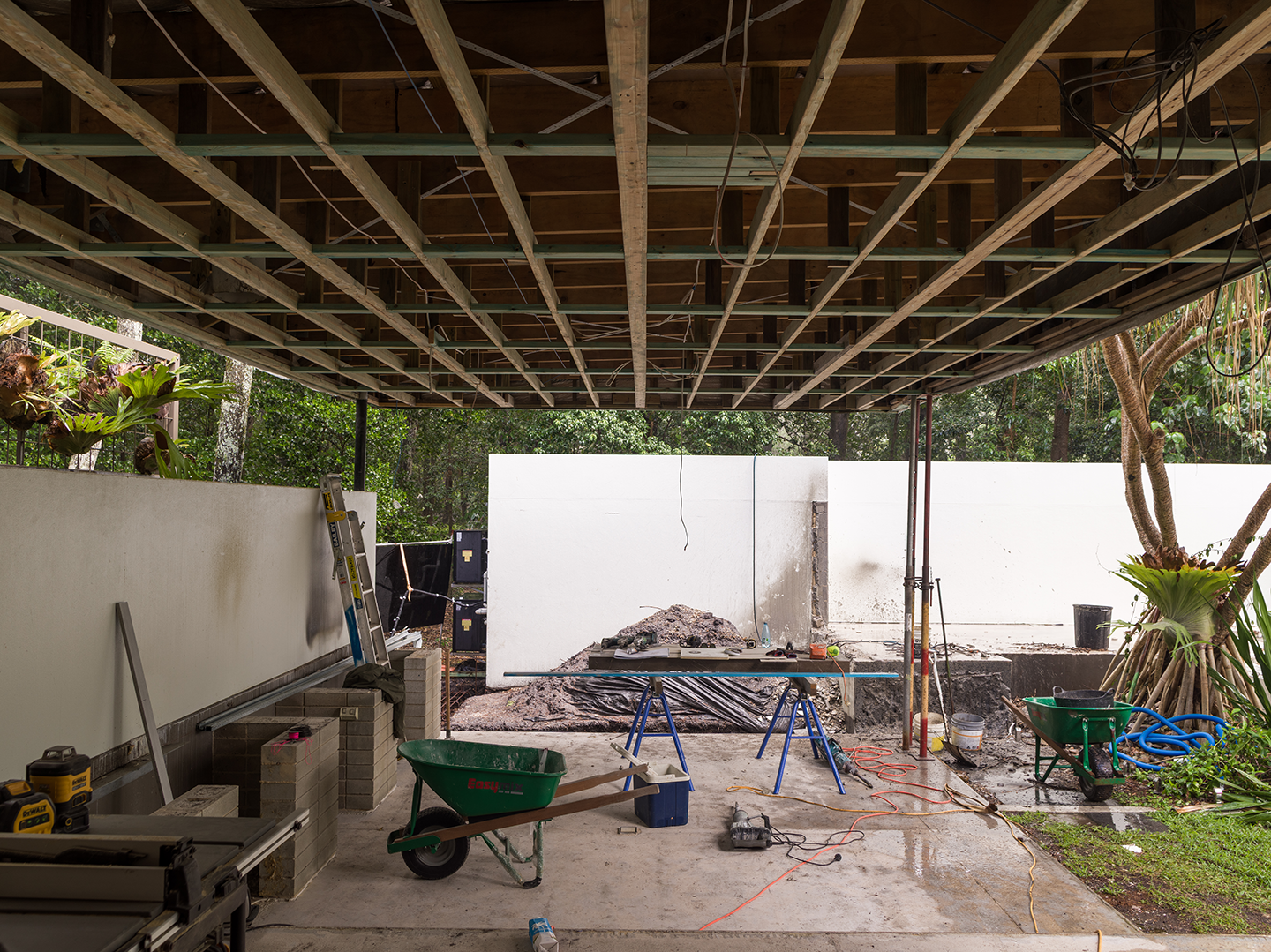 Construction site with exposed ceiling framework, tools, wheelbarrows, and a pile of dirt in the background.