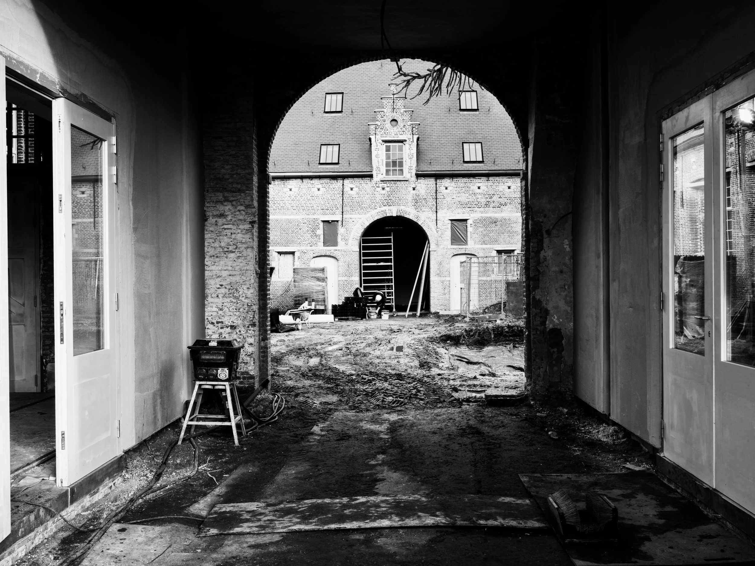 Framed view through a masonry archway looking out toward a historic brick courtyard under renovation.