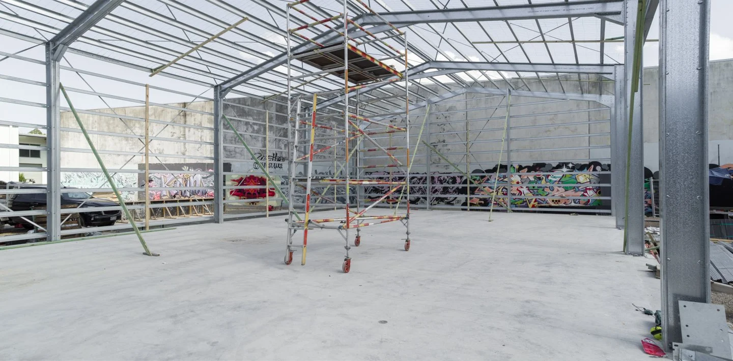 Construction site of a building with metal framework, scaffolding, and graffiti murals on the wall in the background.